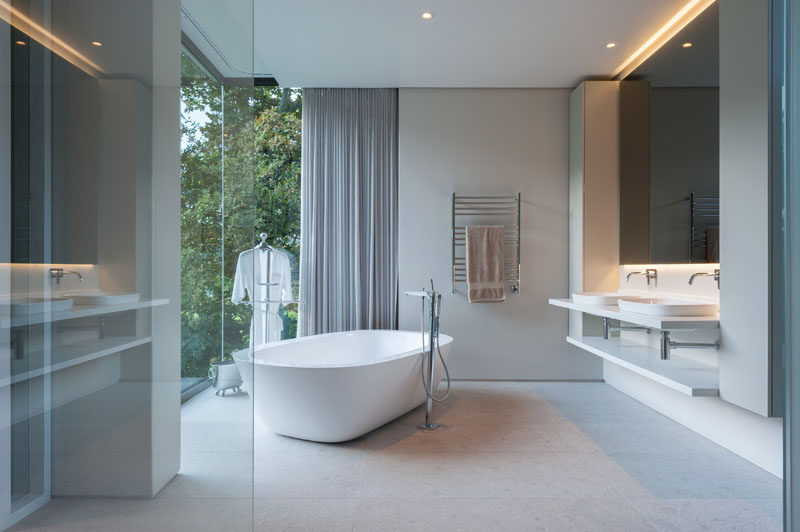 В этой современной ванной комнате зеркало со скрытой подсветкой создает успокаивающую атмосферу, а отдельно стоящая ванна находится напротив окон от пола до потолка, чтобы насладиться прекрасным видом.