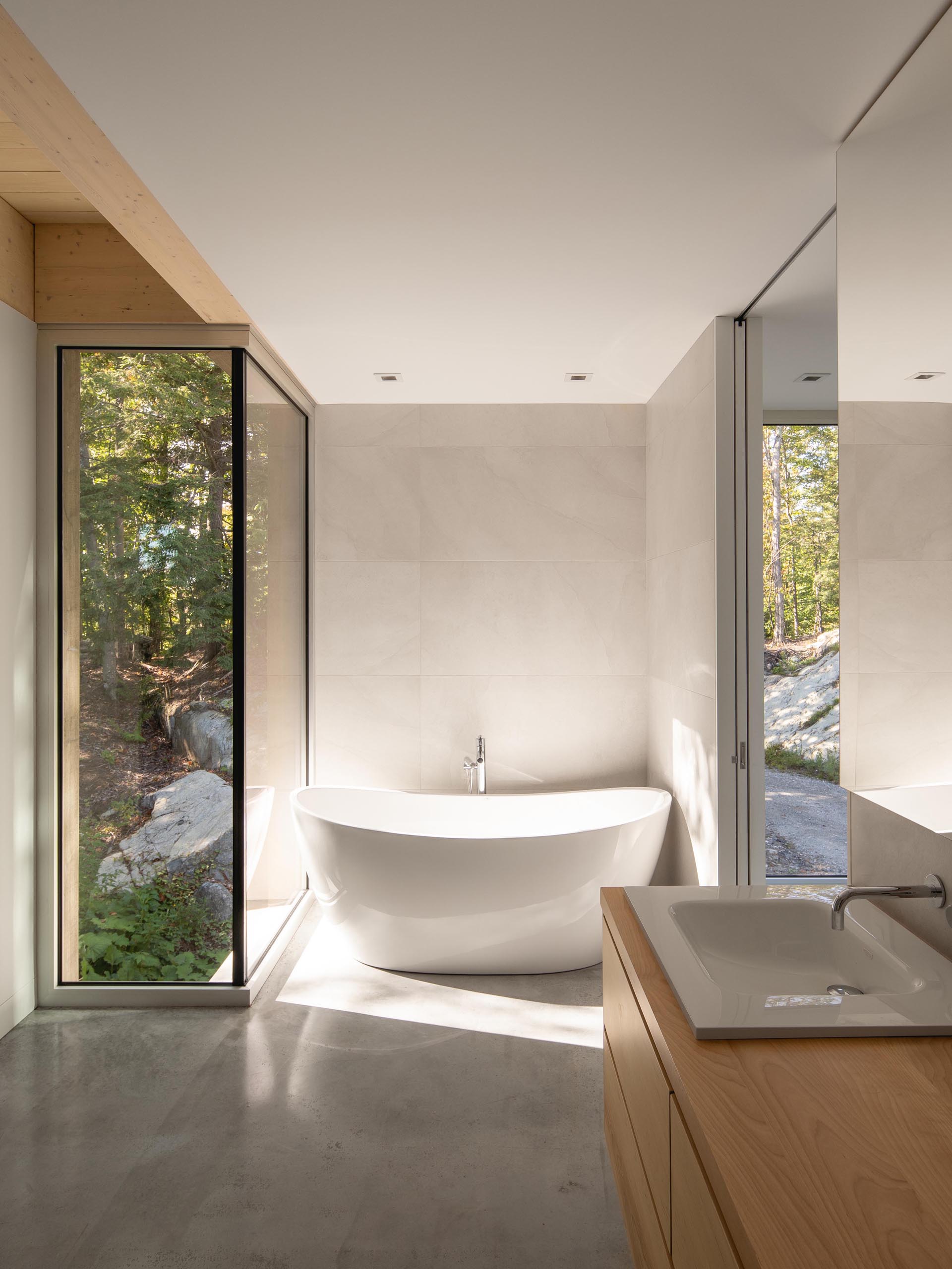 В этой современной ванной комнате есть отдельно стоящая ванна с видом на лес, а деревянный туалетный столик добавляет естественности.