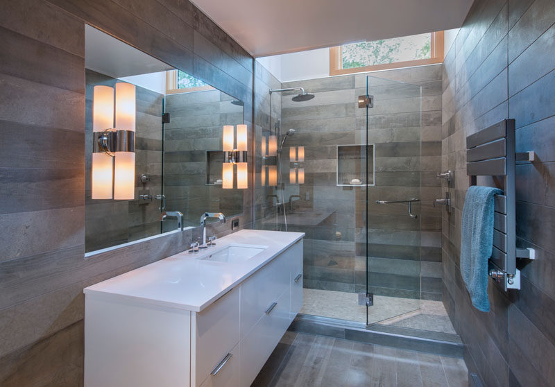 В этой современной ванной комнате серая плитка украшает стены, а стеклянная душевая кабина пропускает свет из окна на туалетный столик.