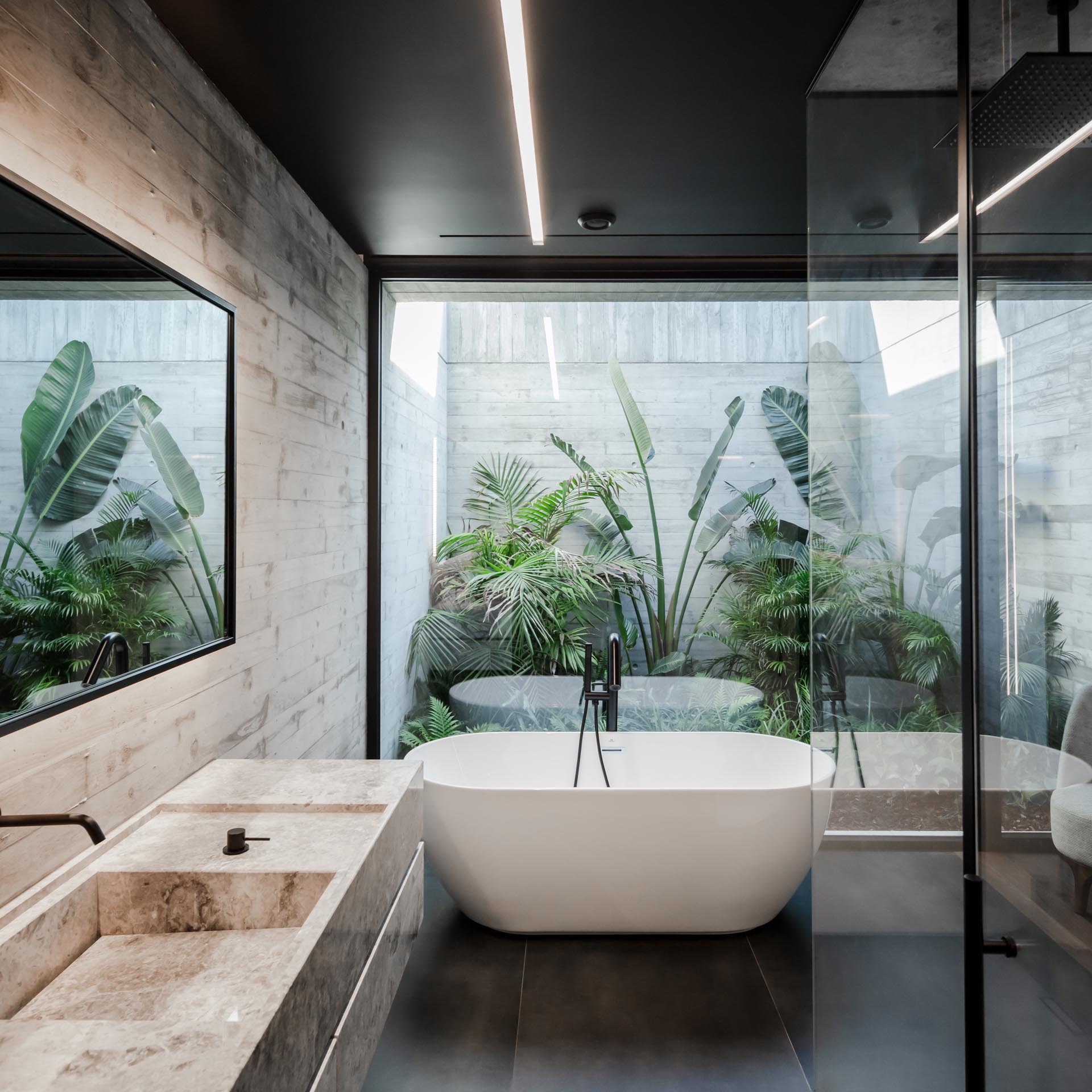 В этой современной ванной комнате за отдельно стоящей ванной есть стеклянная стена, через которую открывается вид на тропический сад.