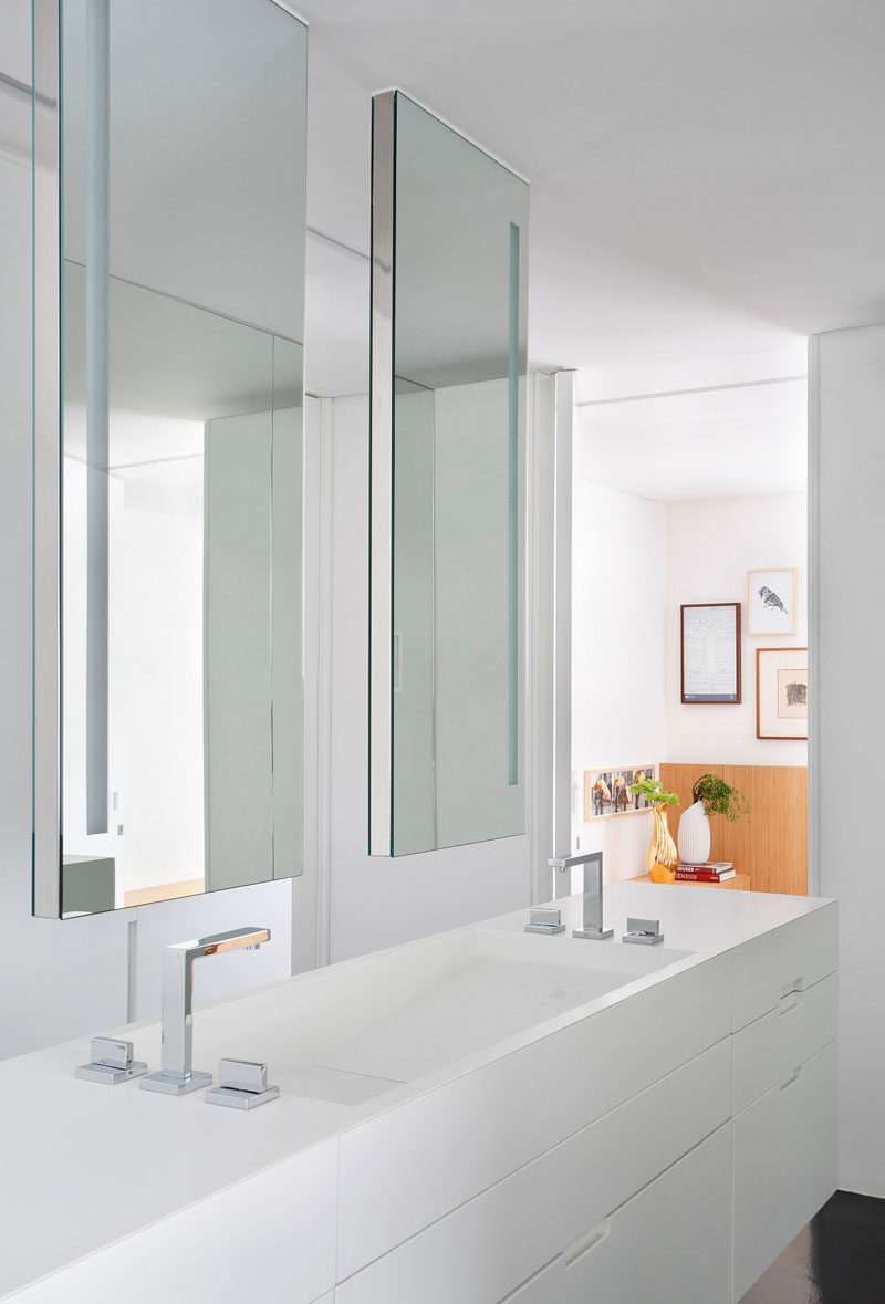 Эта современная ванная комната, которая также служит гардеробной, включает белые столешницы из кориана и двойной туалетный столик с двумя подвесными зеркалами, которые помогают украсить пространство, отражая всю белую мебель.