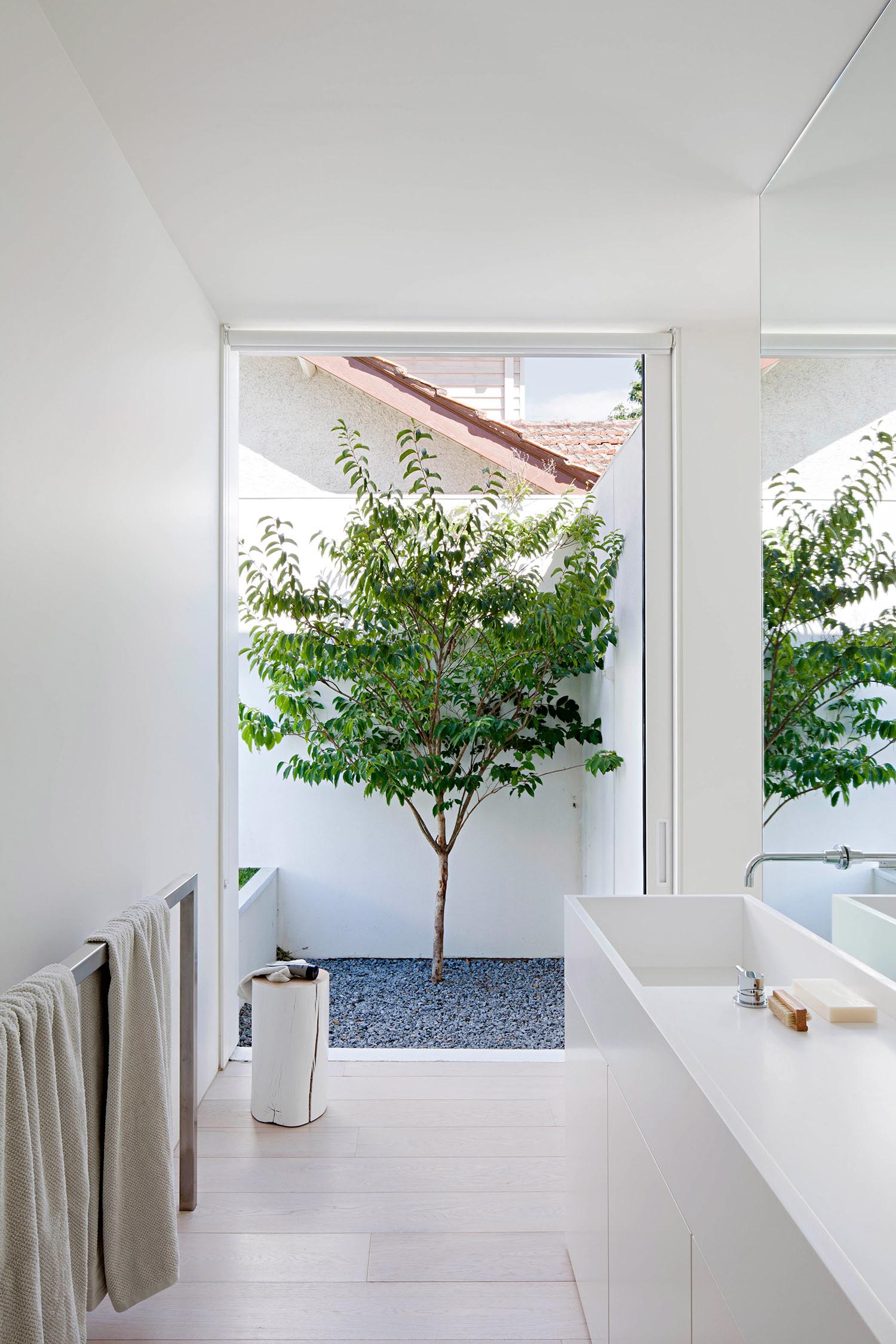 Современная белая ванная комната с большим окном, минималистичным белым туалетным столиком и металлической вешалкой для полотенец.