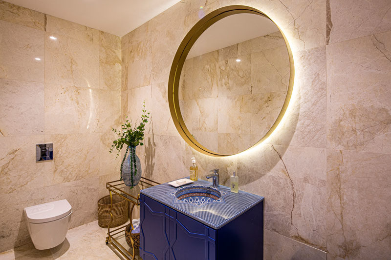 Идеи для ванной комнаты - в этой современной ванной комнате синий туалетный столик имеет декоративную верхнюю часть, в то время как большое круглое зеркало имеет подсветку, а небольшой боковой столик добавляет место для демонстрации вазы. #BathroomIdeas # ModernBathroom #BathroomDesign