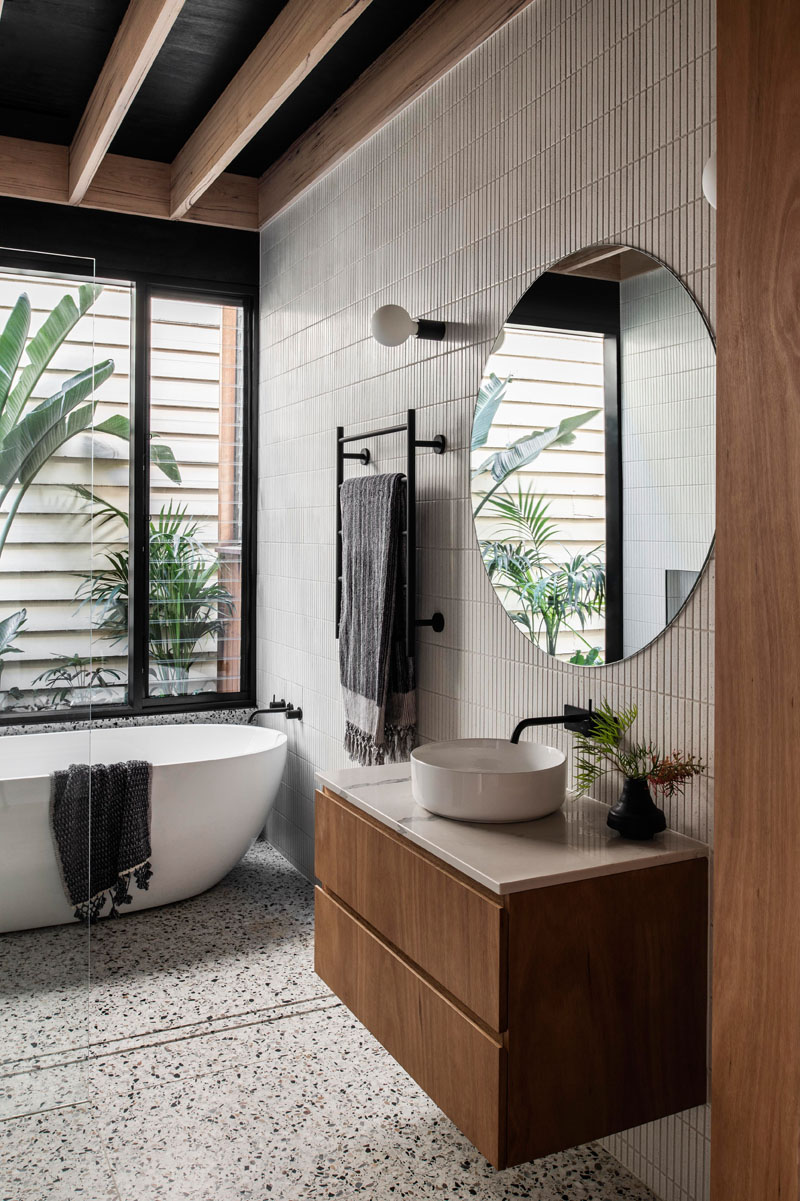 В ванной комнате стены покрыты плиткой, а отдельно стоящая ванна расположена под окном, а стеклянная душевая кабина в минималистском стиле позволяет естественному свету из окна проникать по всей комнате. # Модерн # Дизайн ванной # Плиточные стены # Круглое зеркало