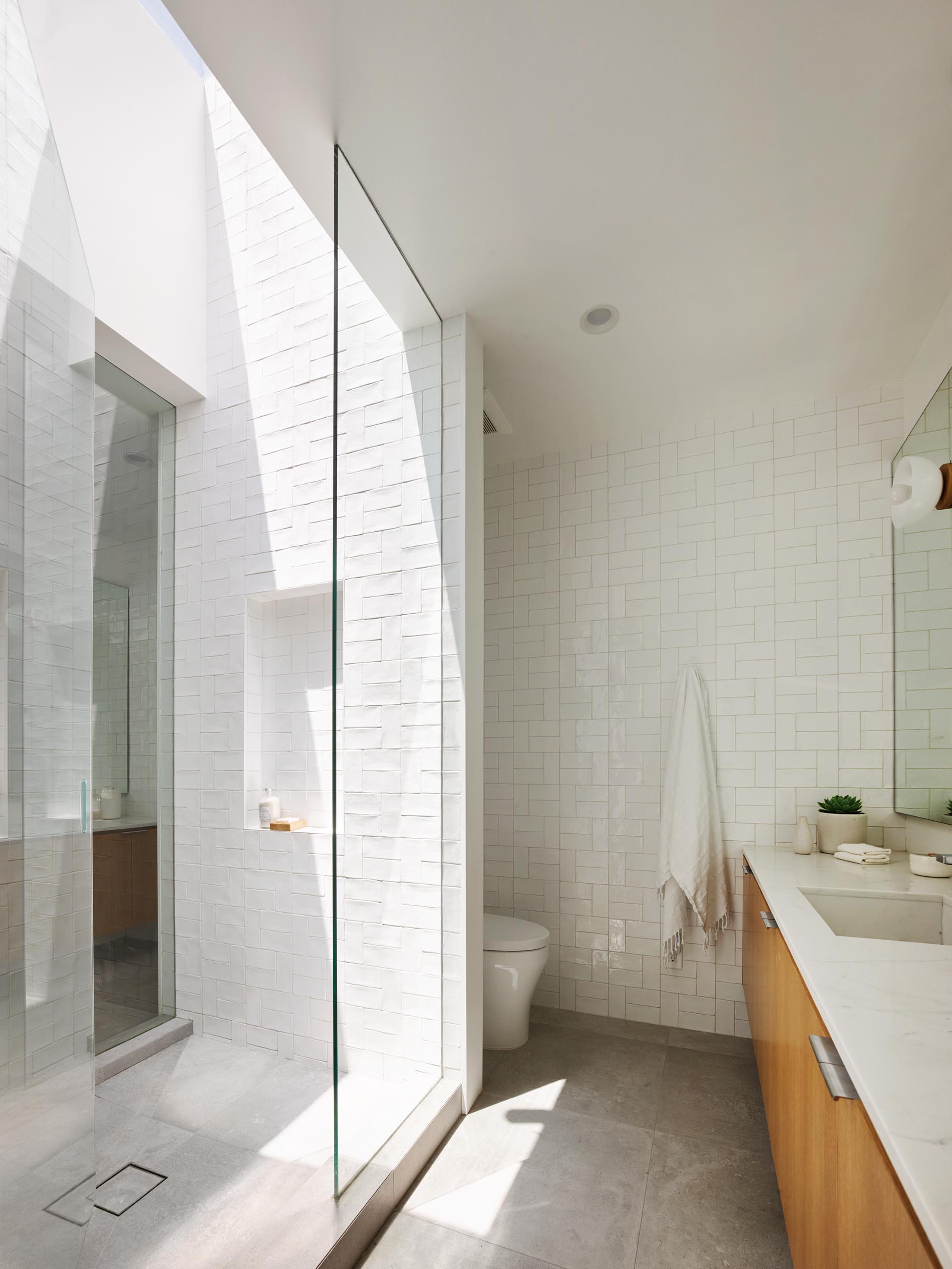 Современная ванная комната с душевой кабиной, облицованной белой плиткой, и потолочным окном, дающим много естественного света.