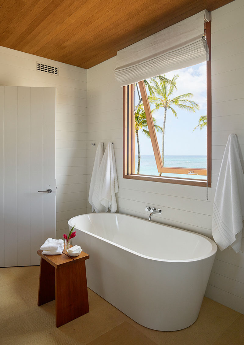 В этой современной ванной комнате пляжного домика отдельно стоящая белая ванна находится под окном с видом на пляж. #ModernBathroom #WhiteAndWood