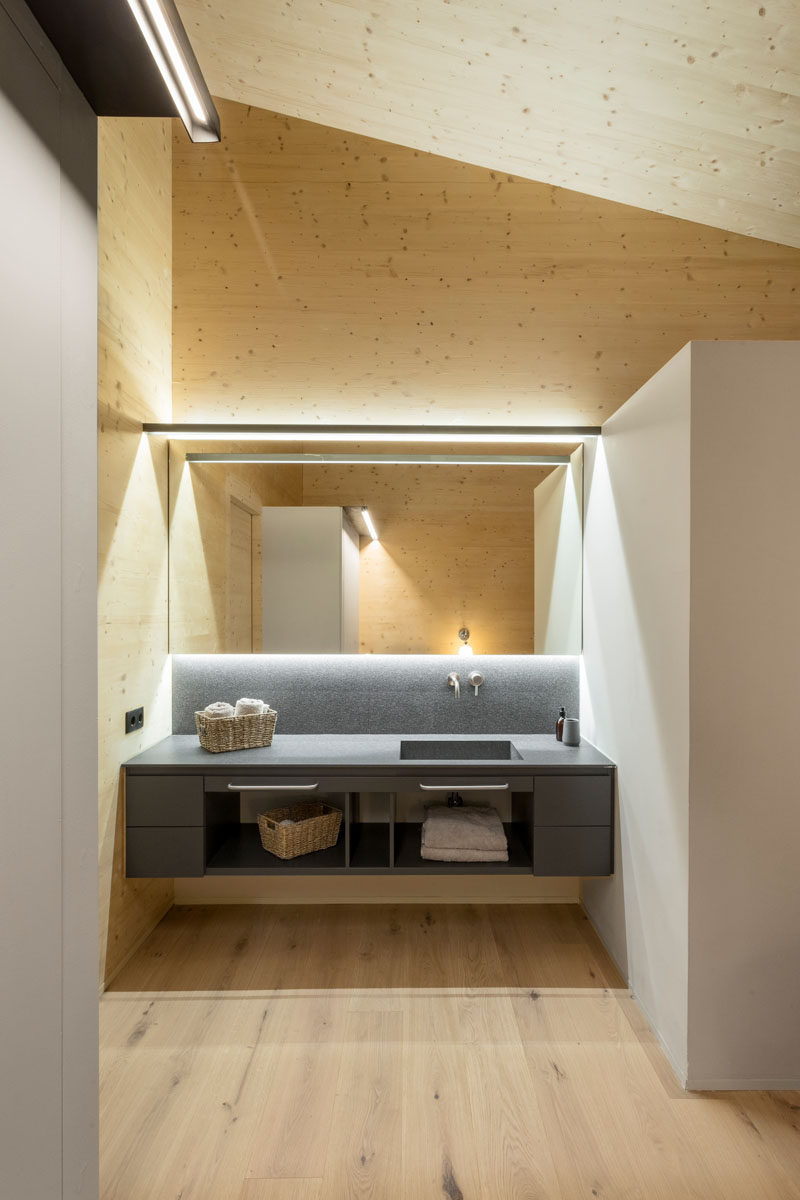 В этой современной ванной комнате серые шкафы выделяются на фоне деревянных стен и потолка, а зеркало с подсветкой и минималистичное освещение подчеркивают тщеславие. # Современная ванная # Освещение # Дизайн ванной
