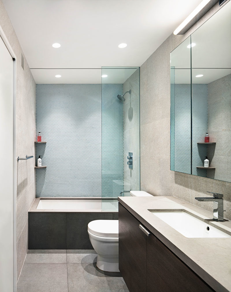 Идеи для ванных комнат - в этой современной ванной комнате светло-голубая плитка была использована для создания мягкой акцентной стены в ванной / душе, а туалетный столик из темного дерева увенчан серой стойкой. #BathroomIdeas # ModernBathroom # VanityIdeas # TileIdeas
