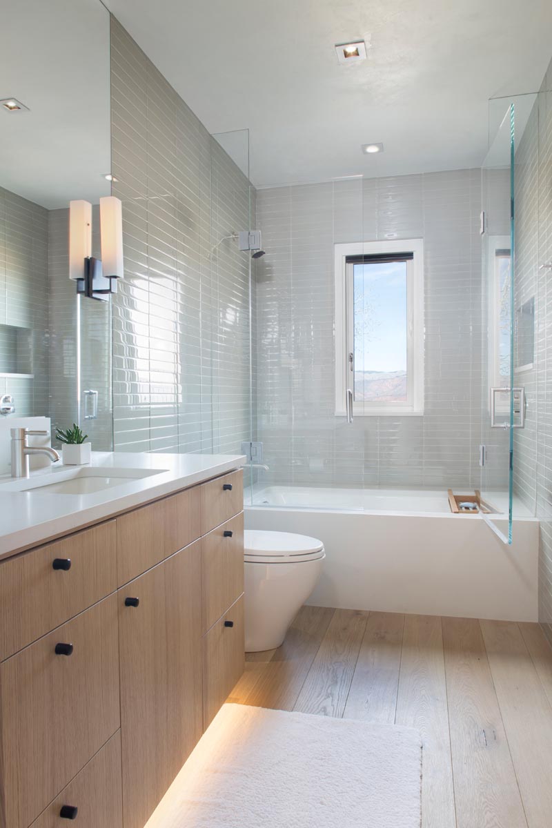 В этой современной ванной комнате светло-серая плитка покрывает стены, а деревянный туалетный столик имеет скрытое освещение под ним, чтобы создать мягкое сияние. # Модерн # Дизайн ванной # Серая плитка