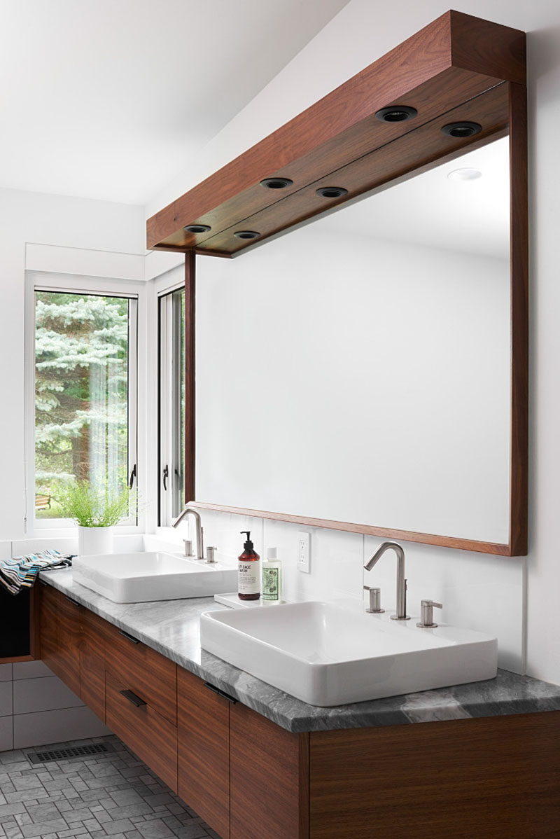  В этой современной главной ванной комнате зеркало в обрамлении темного дерева находится над туалетным столиком с двойной раковиной и каменной стойкой. # МастерВанная # ВаннаяДизайн 