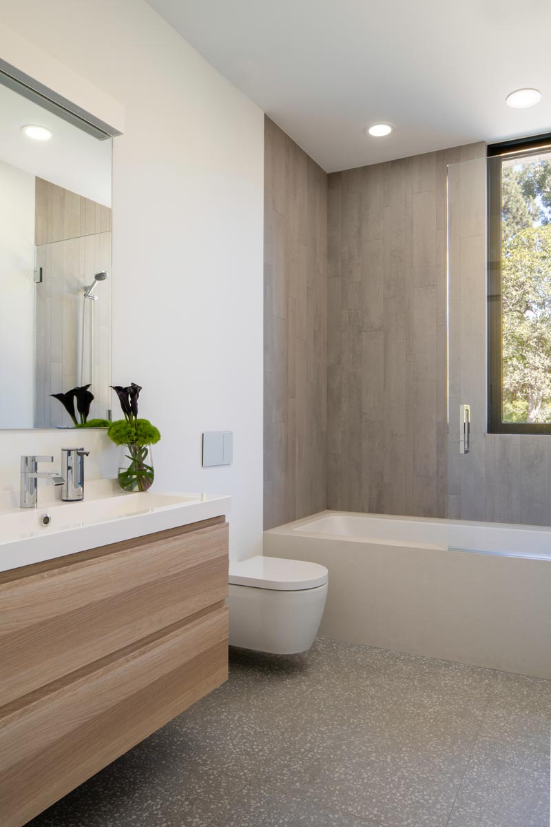 В этой современной ванной комнате простой деревянный туалетный столик имеет белую столешницу, а ванна и душ отделаны плиткой. # ВаннаяДизайн # Современный