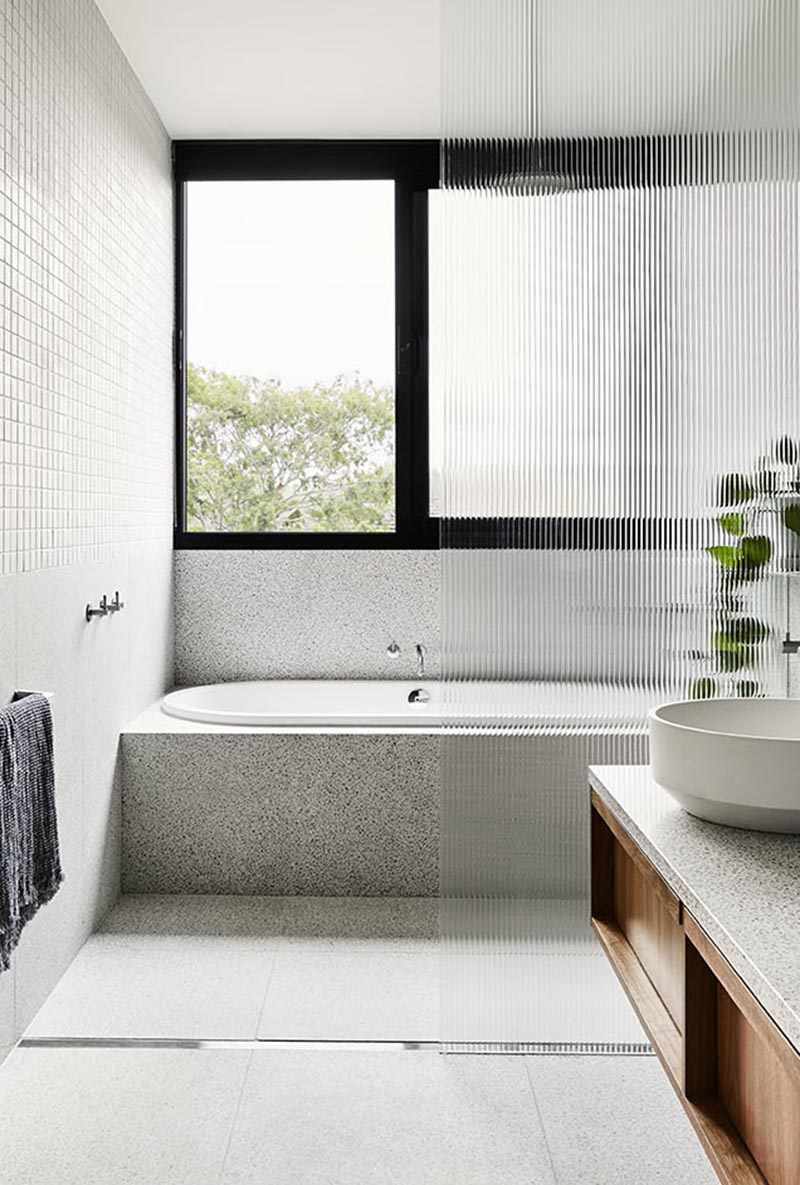 Небольшая серая квадратная плитка покрывает верхнюю половину стен ванной комнаты, в то время как крупноформатная плитка в стиле терраццо демонстрируется на нижней части стен и пола, где находится линейный слив для душа. # Современная ванная # Дизайн ванной # Встроенная ванна # Текстурированная душевая кабина # СерыйВанная