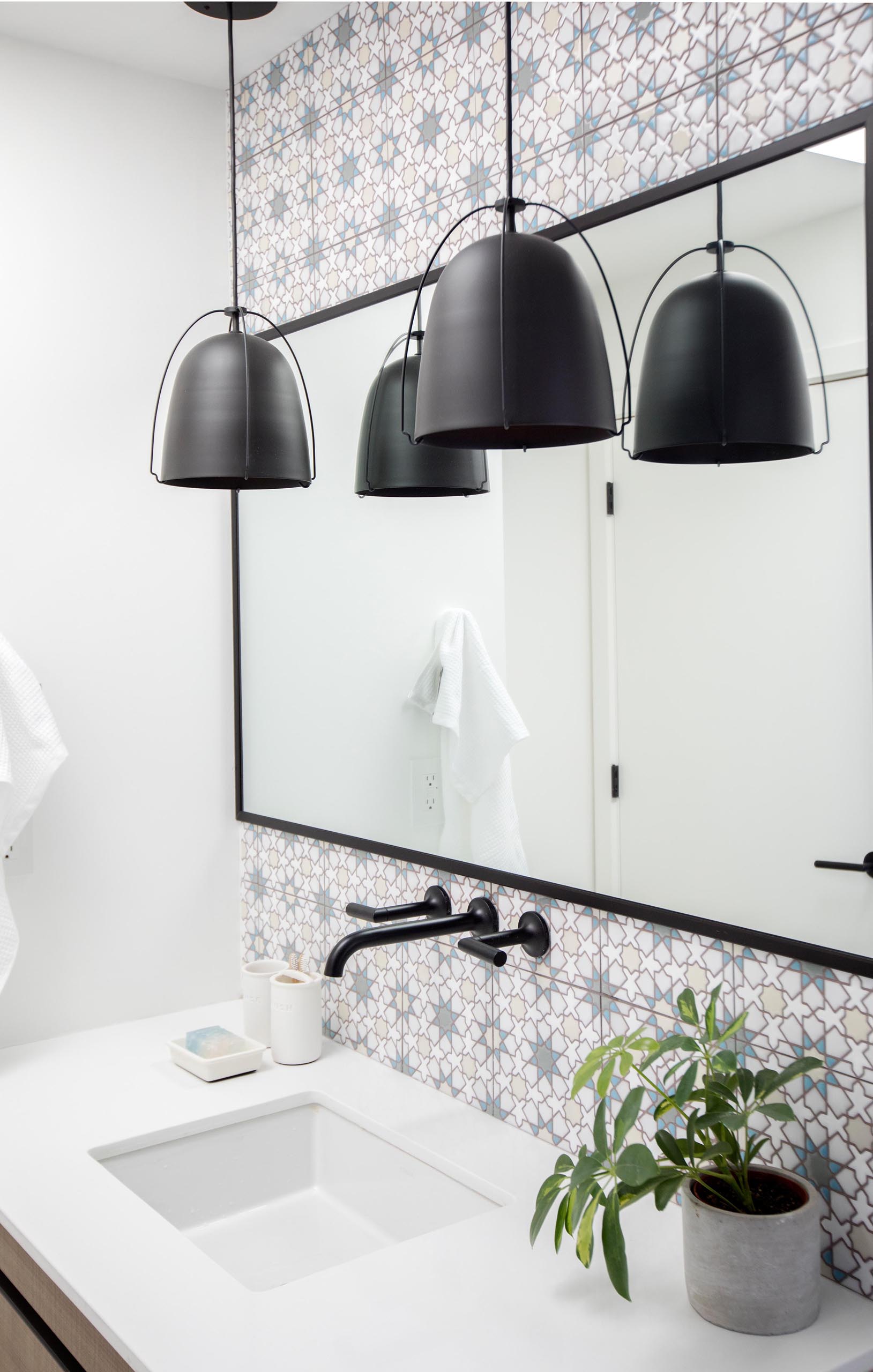 В этой современной ванной комнате узорчатая плитка использовалась для обозначения туалетного столика, а черные подвесные светильники дополняют черную раму зеркала и карниз для штор для душа.
