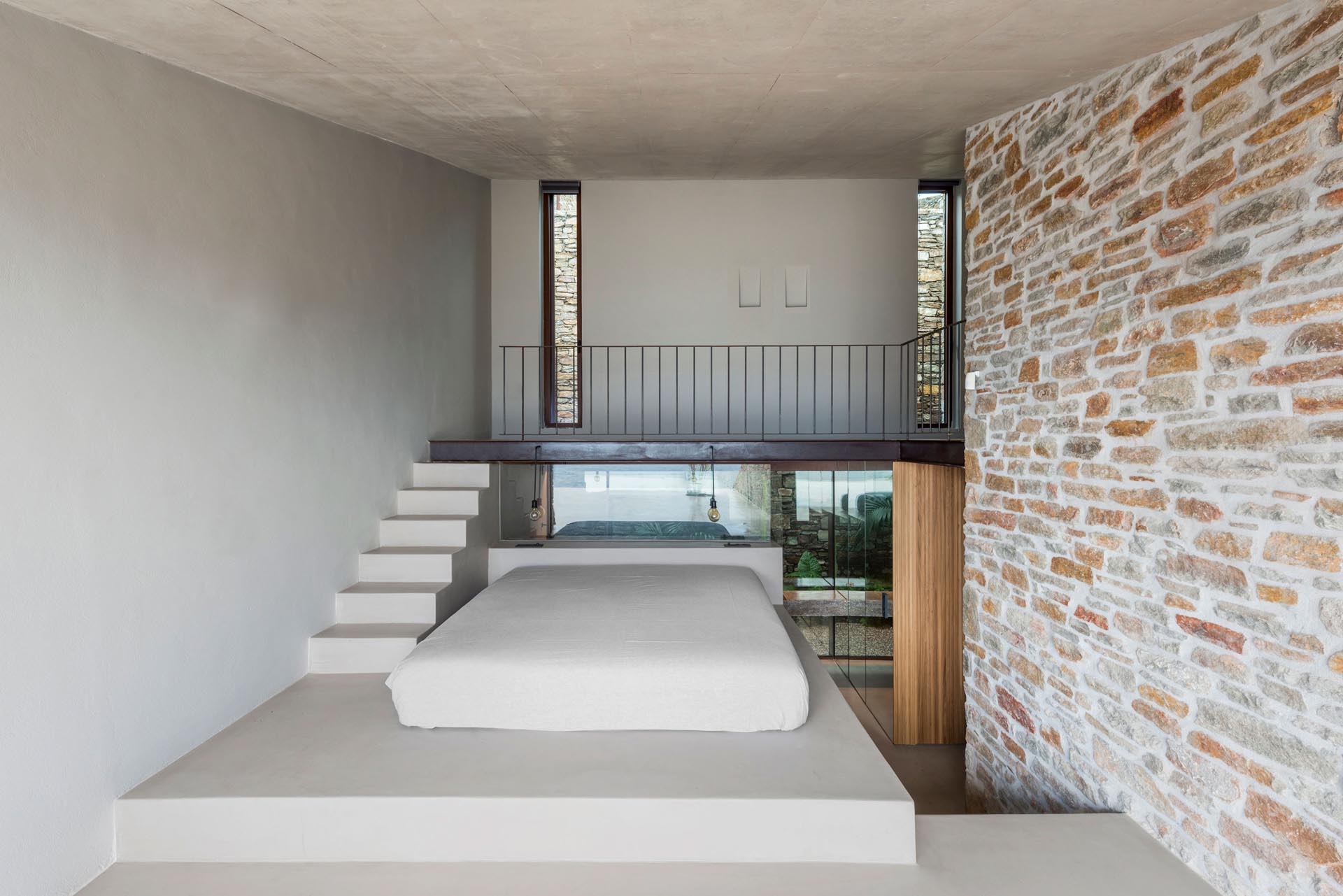 Спальня в стиле минимализма с кроватью, приподнятой на платформе, откуда открывается вид на воду.