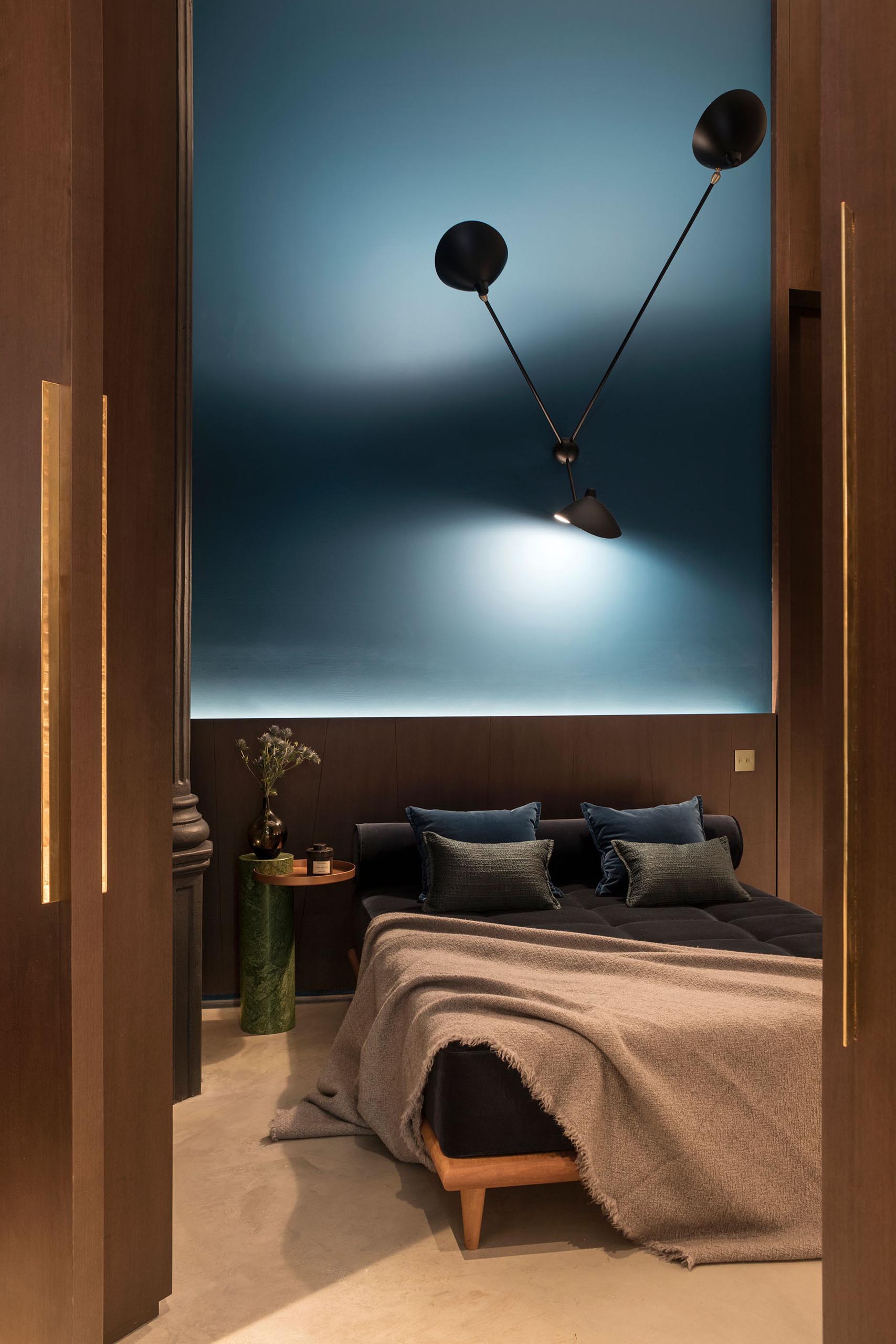 Современная спальня с высокими потолками и яркой матовой синей стеной.