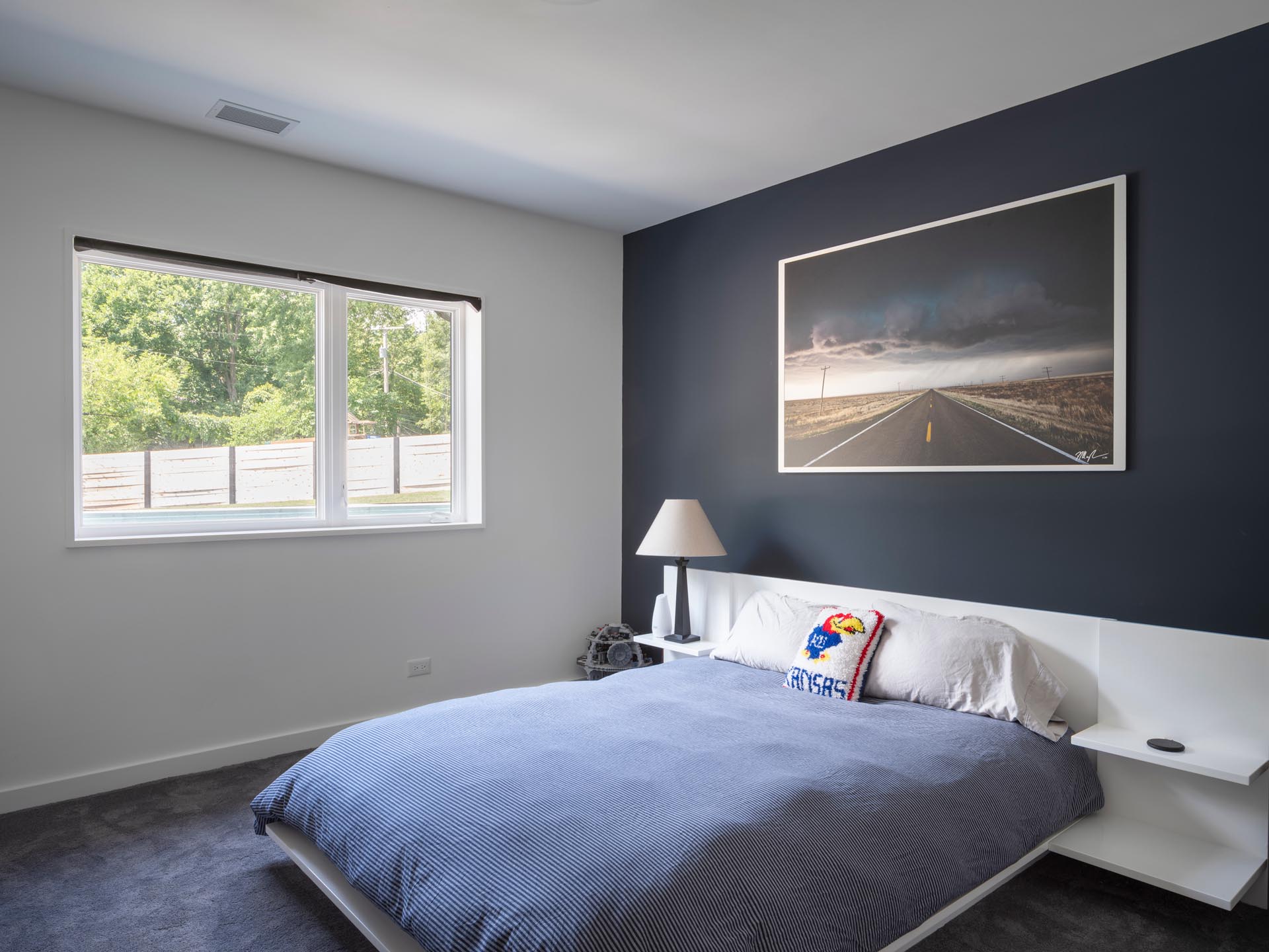 Современная спальня с матовой черной акцентной стеной, контрастирующей с белым каркасом кровати и тумбочками.