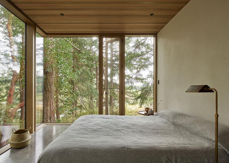 В этой спальне в стиле минимализма окна от пола до потолка обеспечивают непрерывный вид на окружающие деревья. # СовременнаяСпальня # Окна # ДеревянныйПотолок