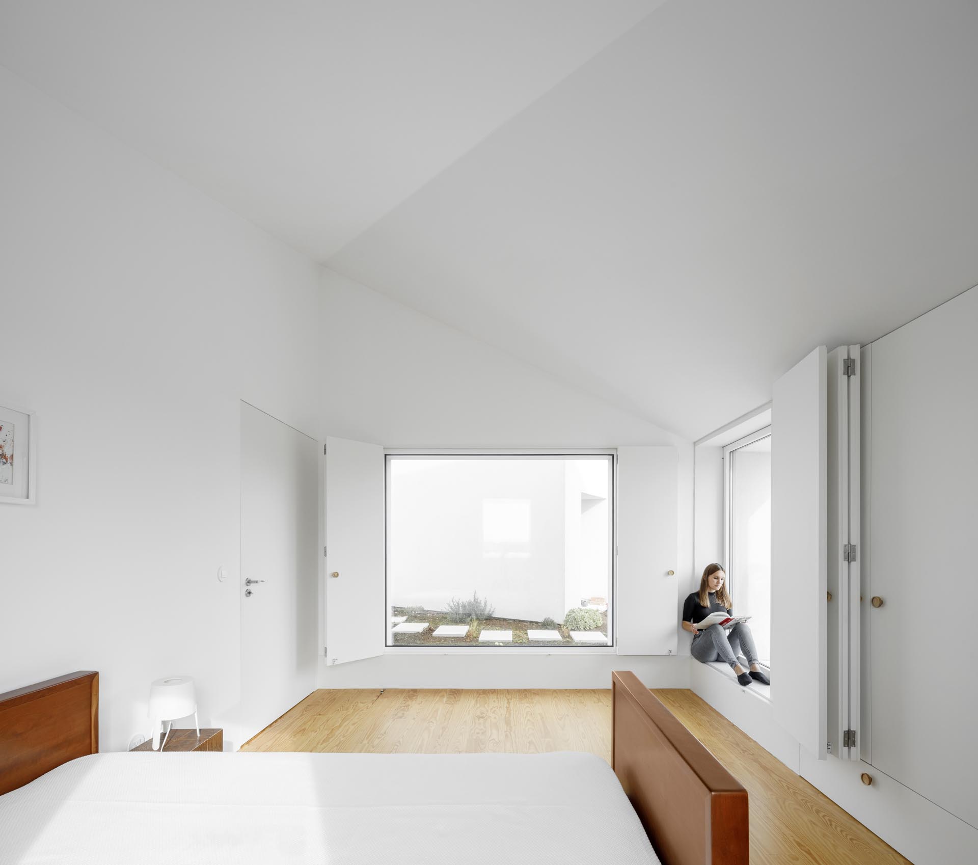 Современная спальня с мебелью в стиле минимализма и складными оконными ставнями.