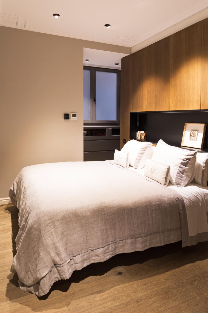 В этой современной главной спальне за кроватью есть акцентная стена из дерева, которая включает в себя матовую черную нишу для полок с подсветкой.