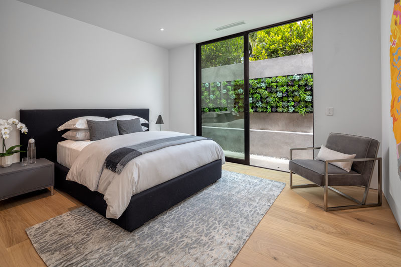 Современная гостевая спальня с раздвижной стеклянной дверью, которая ведет в небольшое открытое пространство с сочными стенами.