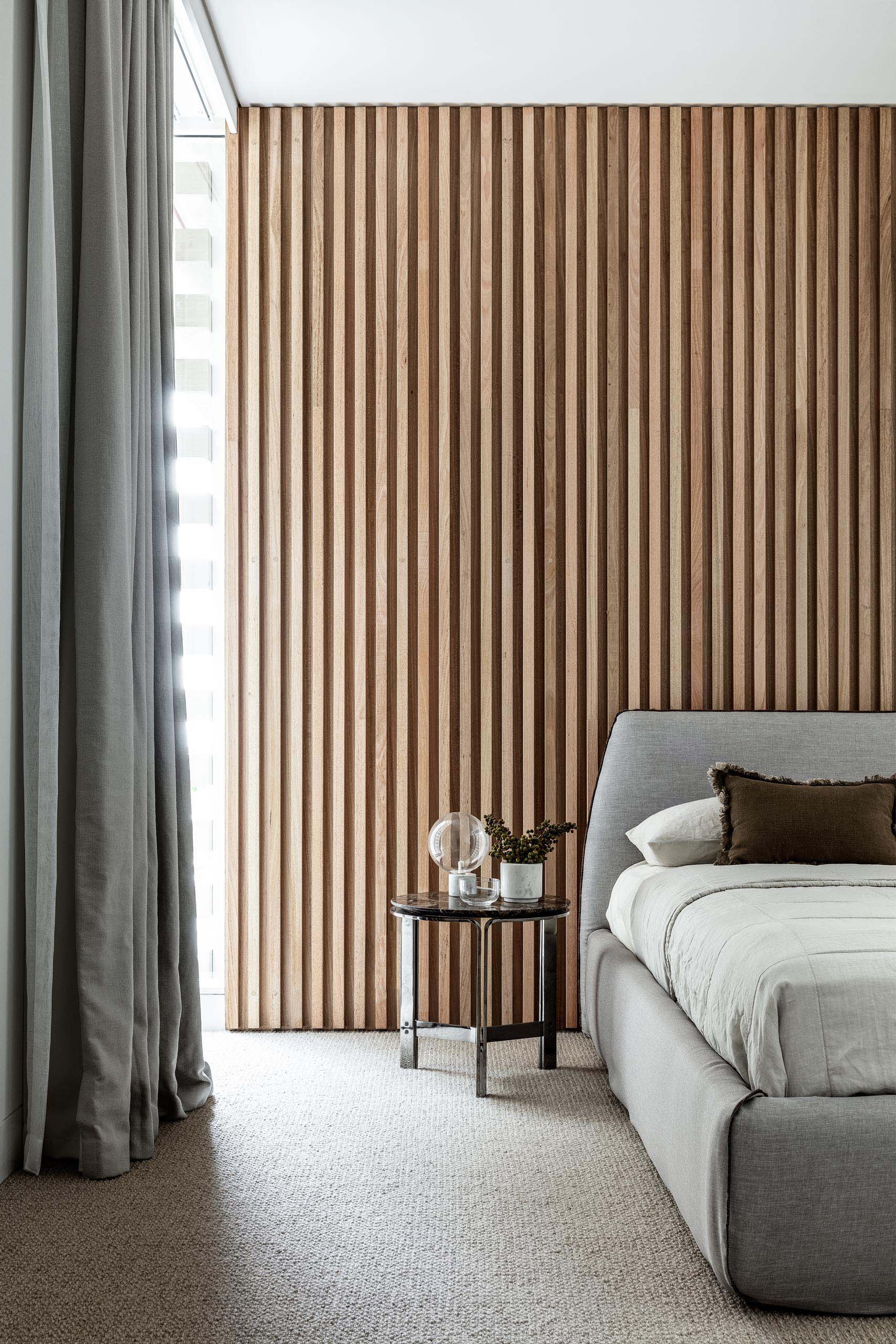 В этой современной спальне деревянная реечная стена была использована для создания акцентной стены за серой мягкой кроватью.