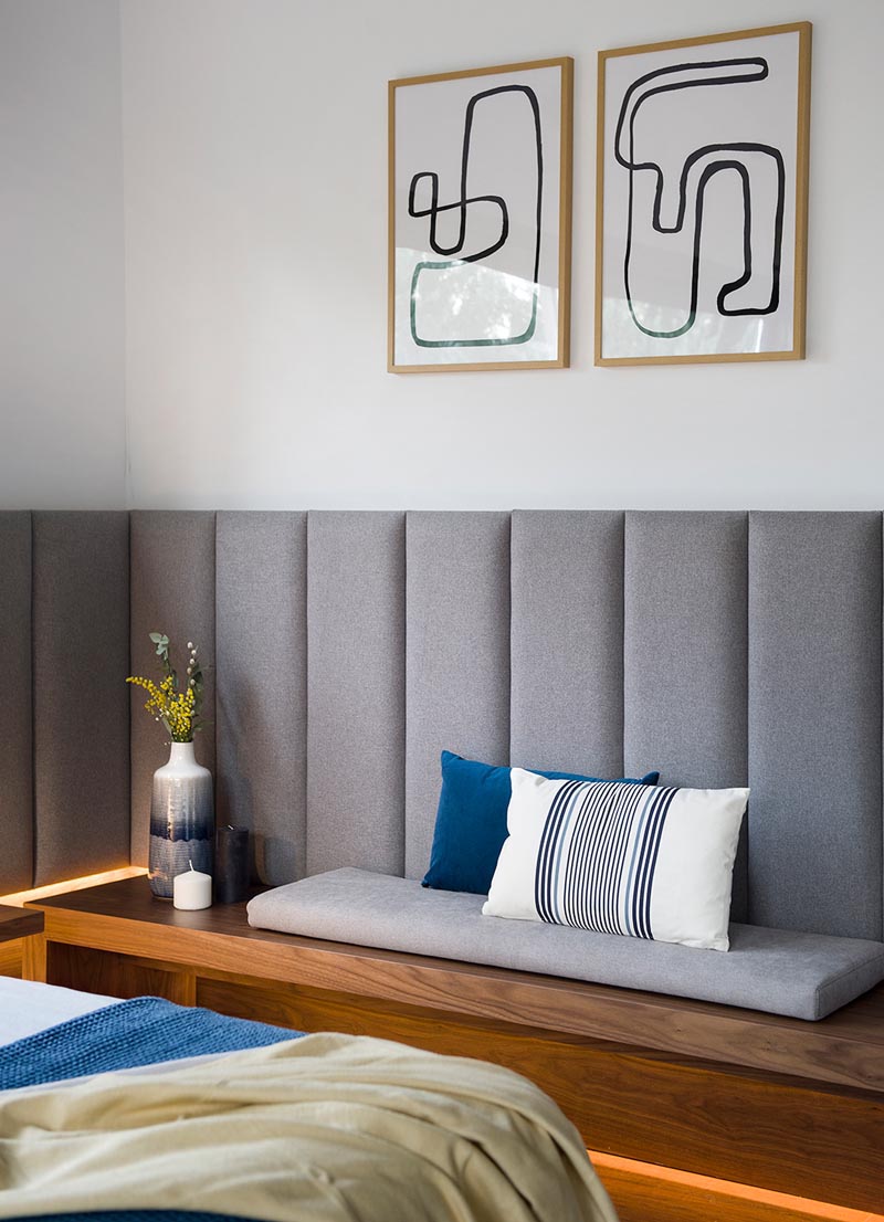 Современная деревянная скамья с серой подушкой и минималистским рисунком на стене выше.