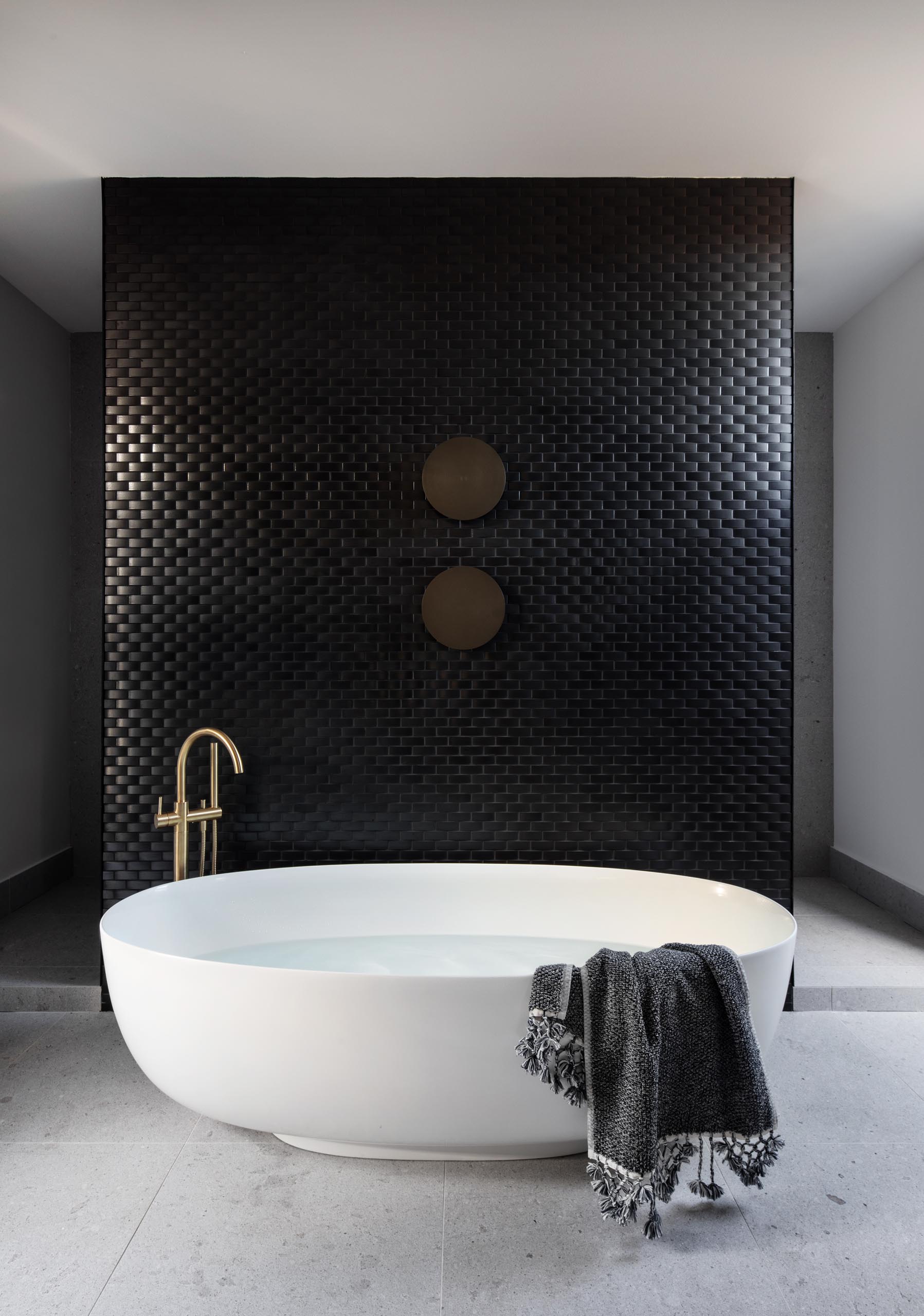 Современная ванная комната с акцентом на стене из черной плитки, которая служит фоном для большой овальной отдельно стоящей ванны.