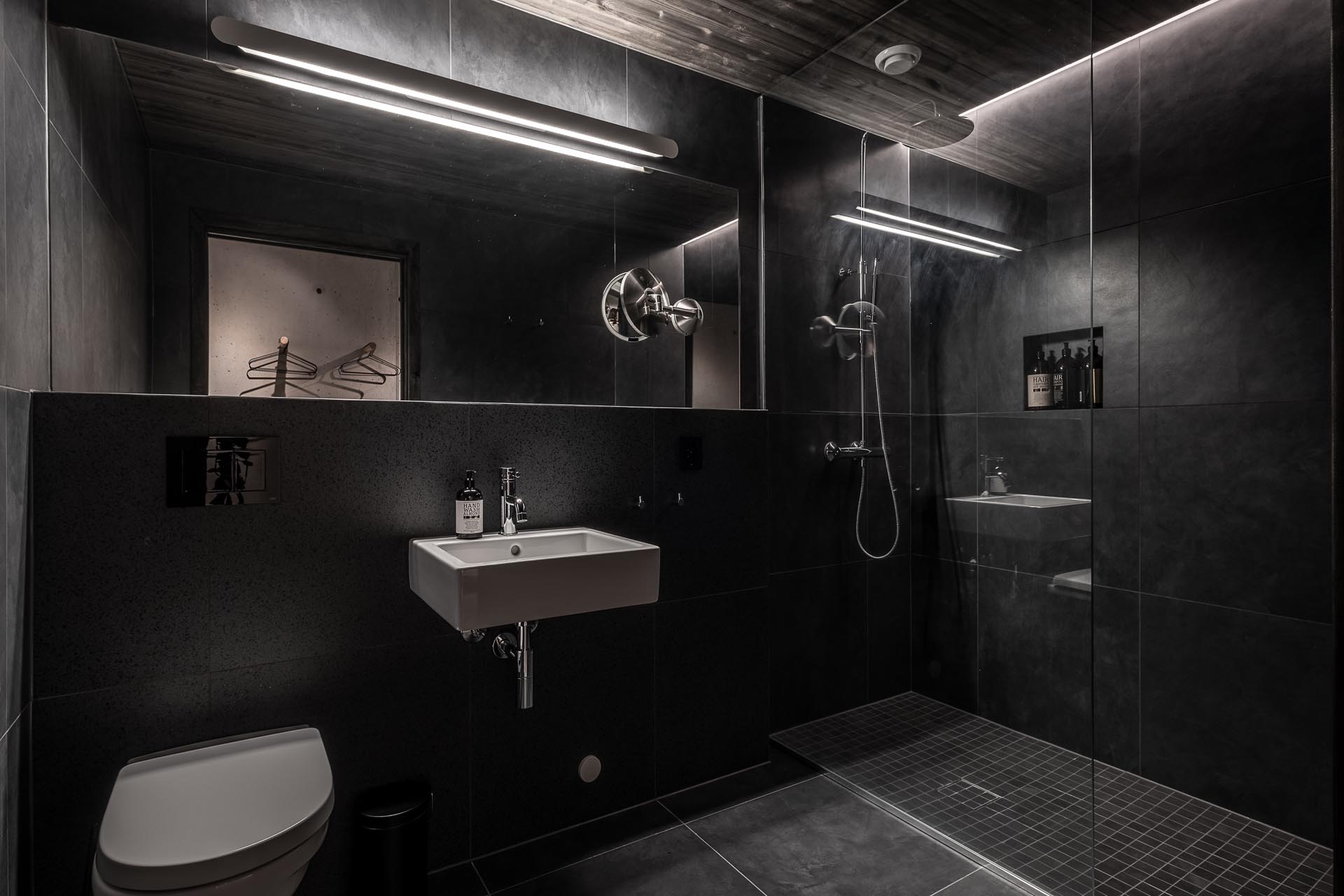 В этой темной ванной комнате широкоформатная черная плитка и освещение были использованы для создания драматического образа.