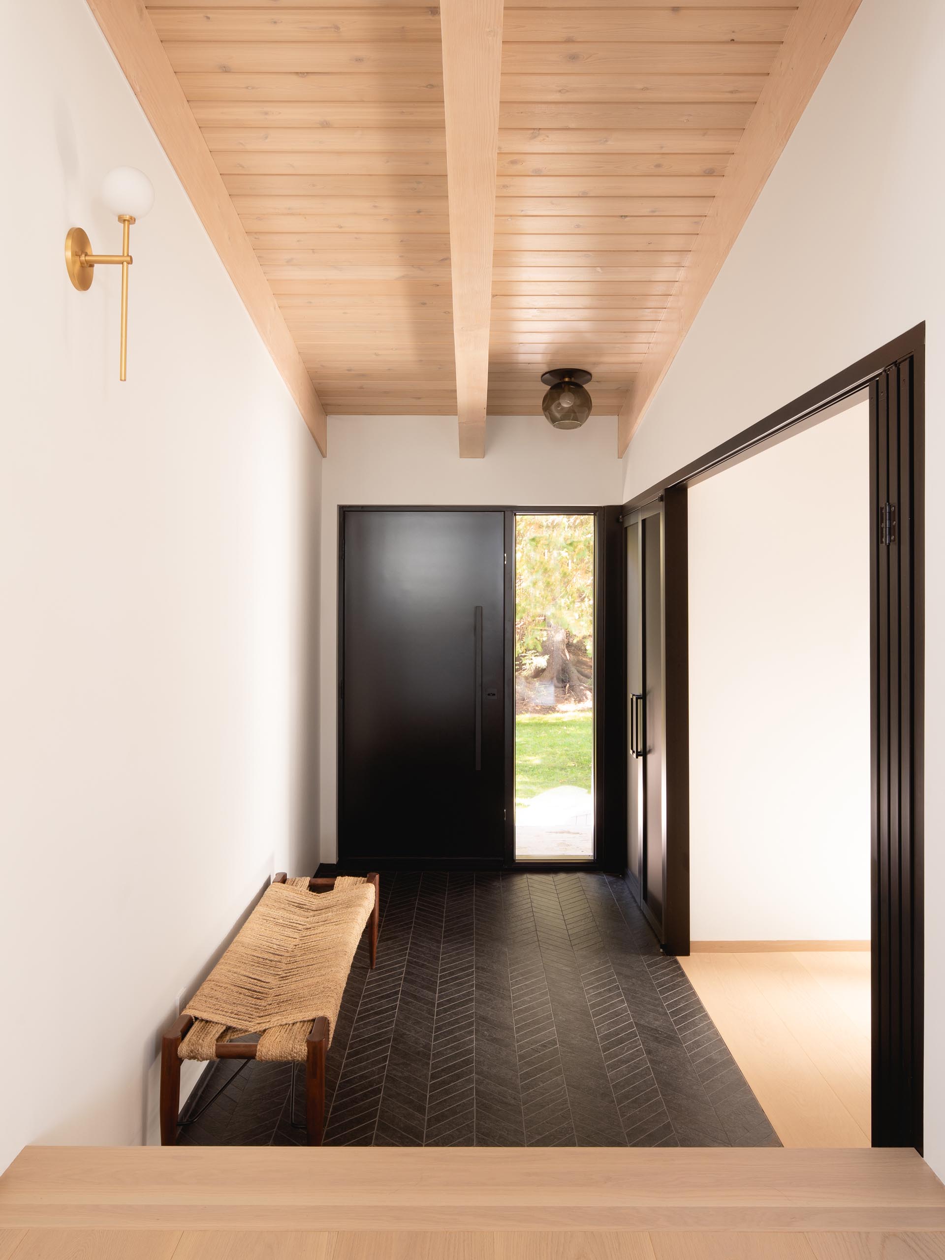 Этот современный вход демонстрирует потолок из светлого дерева, а пол выложен черной плиткой с шевронным узором.
