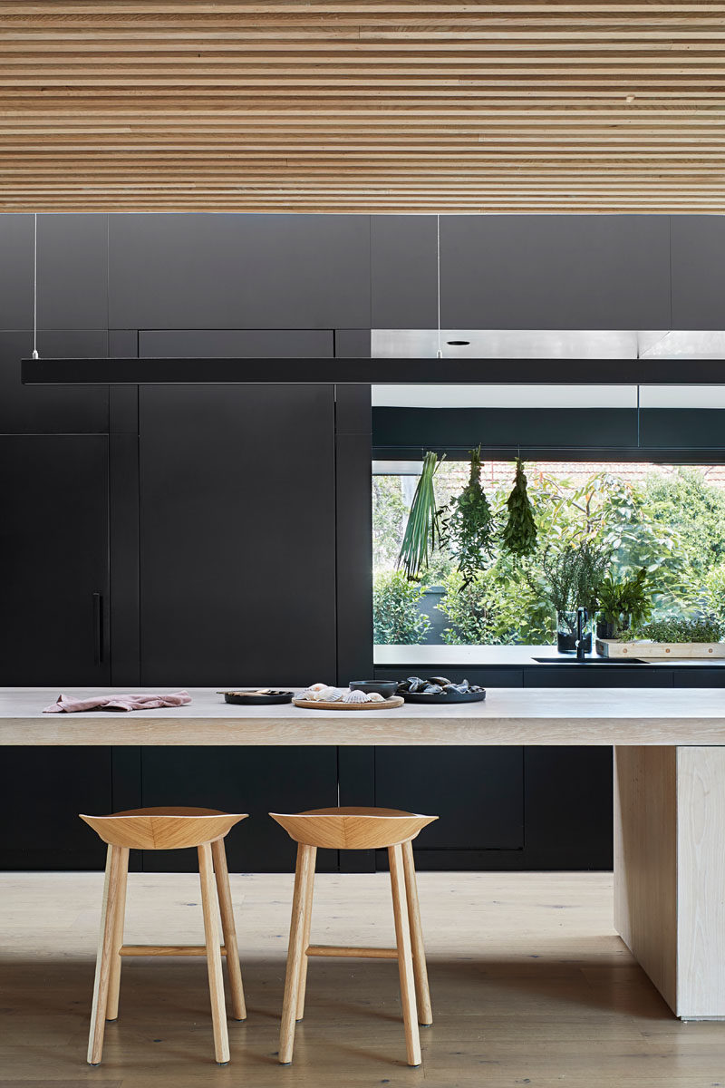 Идеи для кухни - на этой современной кухне минималистичные черные шкафы выстроились вдоль стены, а большой остров обеспечивает достаточно места для стойки и места для сидения. Пустота в шкафах позволяет соединить кухню и кладовую, расположенную за шкафами. #KitchenIdeas #BlackKitchen #KitchenDesign #ModernKitchen