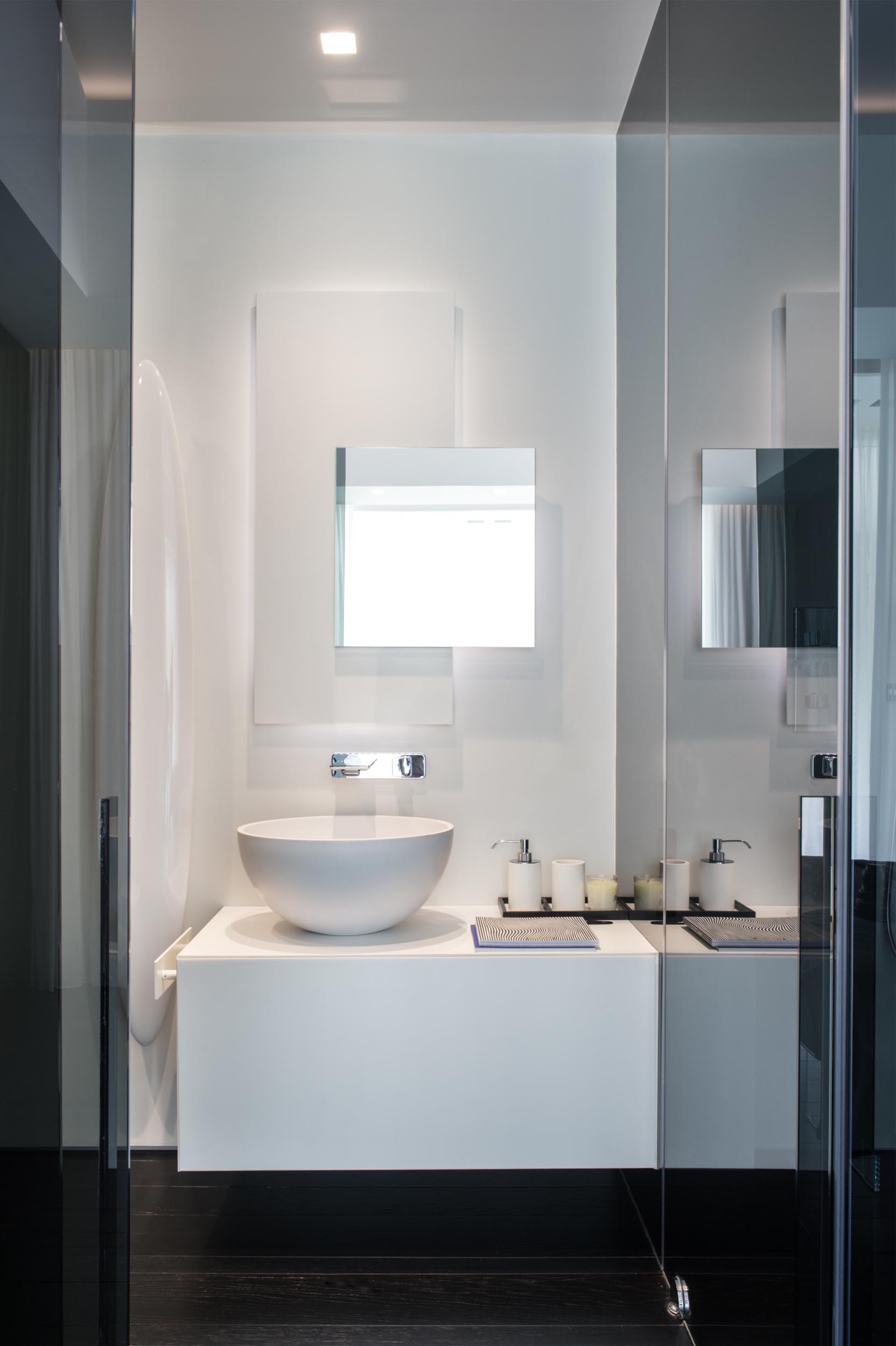 Современная ванная комната с белым туалетным столиком, зеркалом с подсветкой и контрастным черным полом.