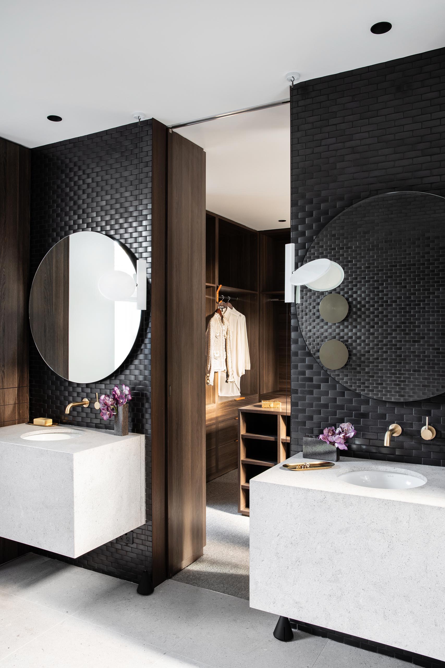 В главной ванной комнате стены покрыты черной плиткой, а круглые зеркала висят над белыми туалетными столиками с раковинами под ними.