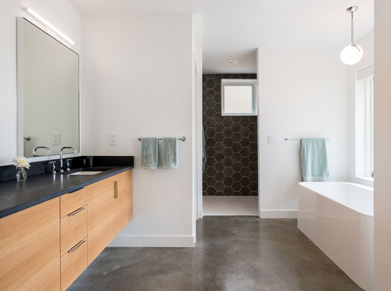 В этой современной ванной комнате белые стены сочетаются с темно-серой шестиугольной плиткой, бетонным полом и деревянным туалетным столиком с темной столешницей. # СовременныеВанная # Серая плитка