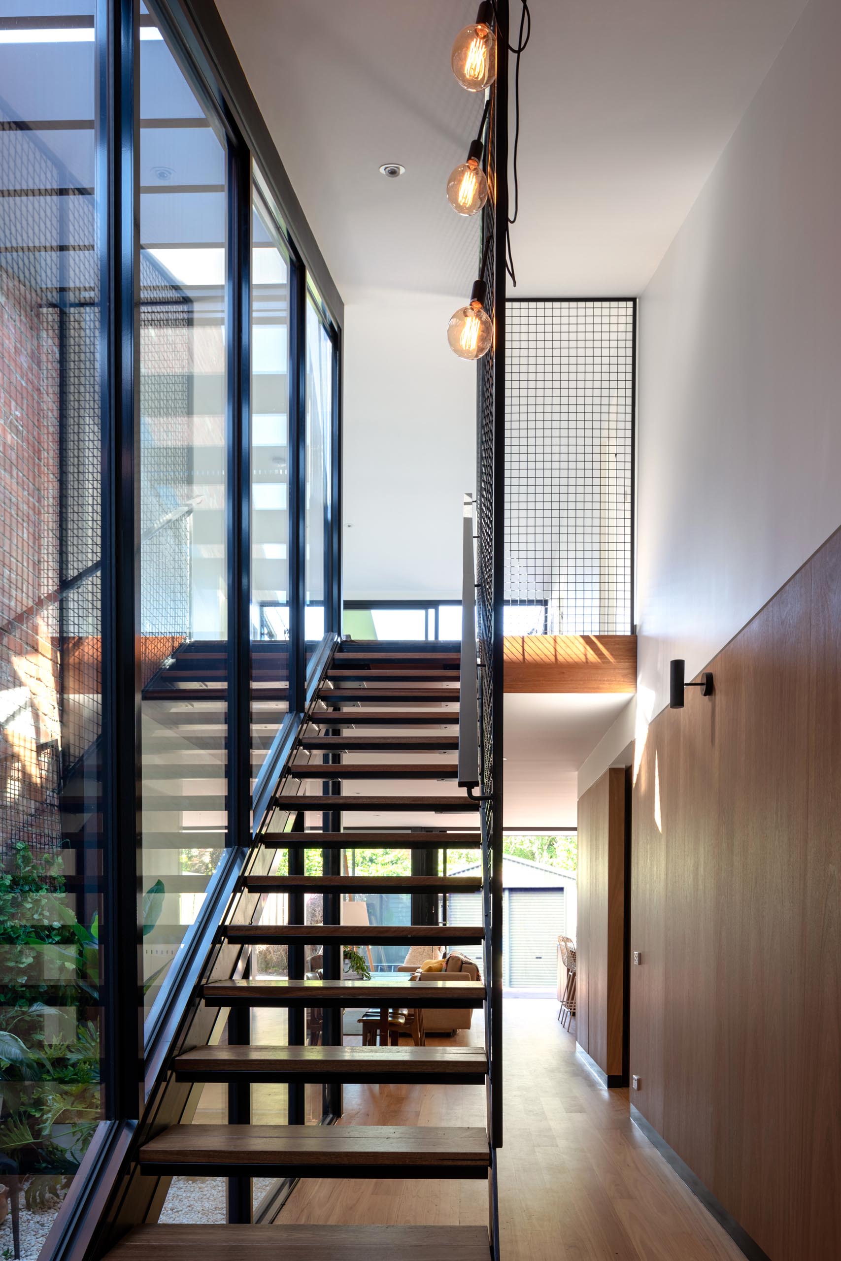 Современная лестница из дерева и стали, идущая вдоль стеклянной стены.
