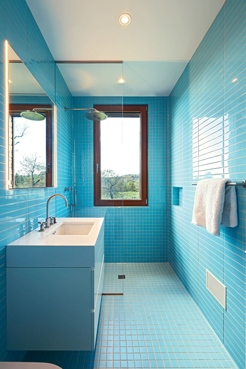 В этой современная ванная комната ярко-голубая прямоугольная и квадратная плитка покрывает стены и пол, контрастируя с деревянной оконной рамой и белым туалетным столиком. # СинийВанная # Современная # ВаннаяДизайн 