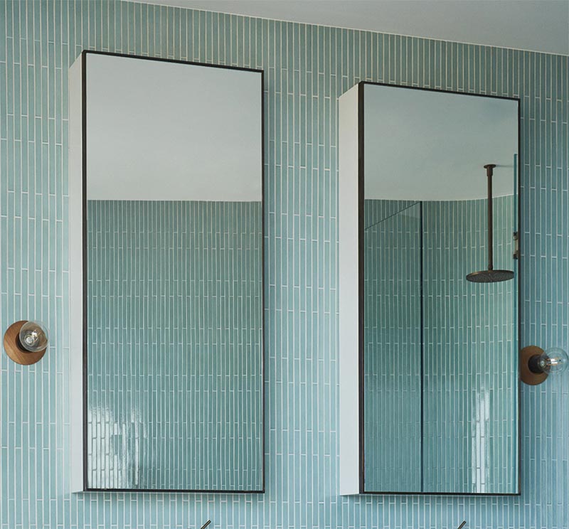 Над туалетным столиком в этой современной ванной комнате стоит дуэт вертикальных зеркал в черной раме. К каждому зеркалу примыкает простой бра с деревянным основанием и открытой лампочкой. # Зеркала для ванной # Модерн #BlueTIles # Дизайн для ванной
