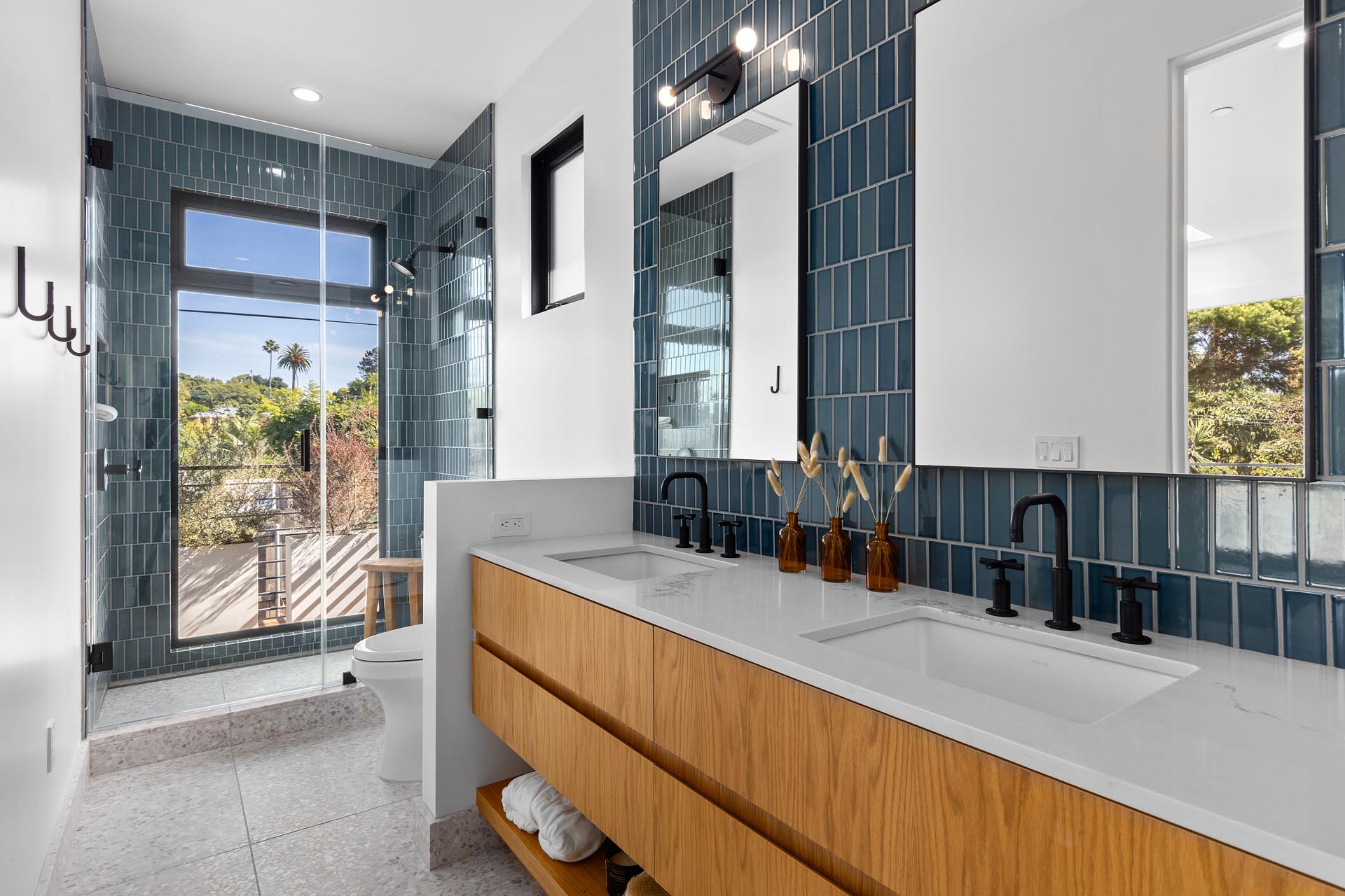 В этой современной ванной комнате стены и душевая кабина отделаны синей плиткой, а также есть деревянный туалетный столик с двойной раковиной.