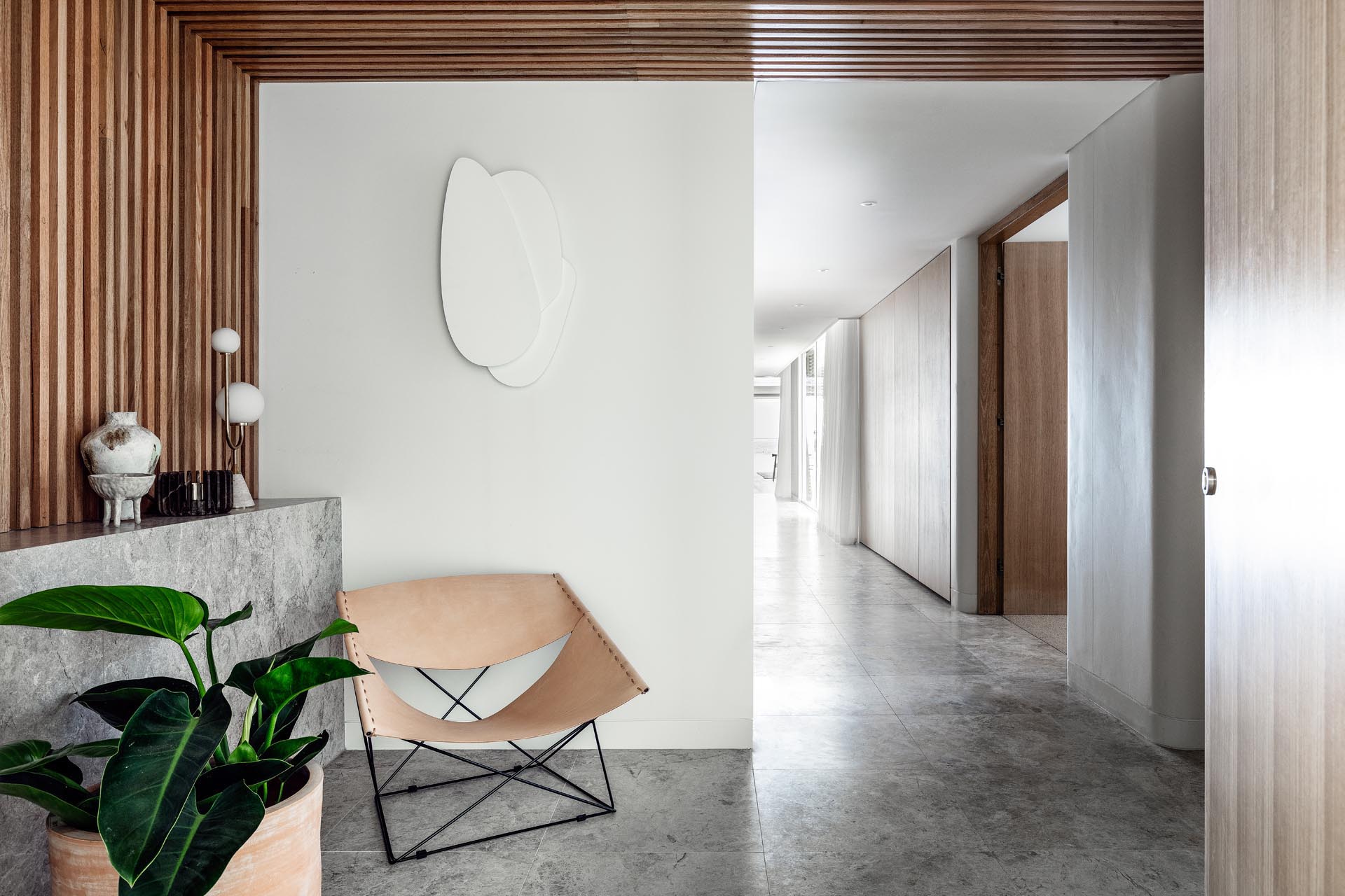 Современная прихожая с кожаным креслом и стеной из деревянных реек, переходящей в потолок.