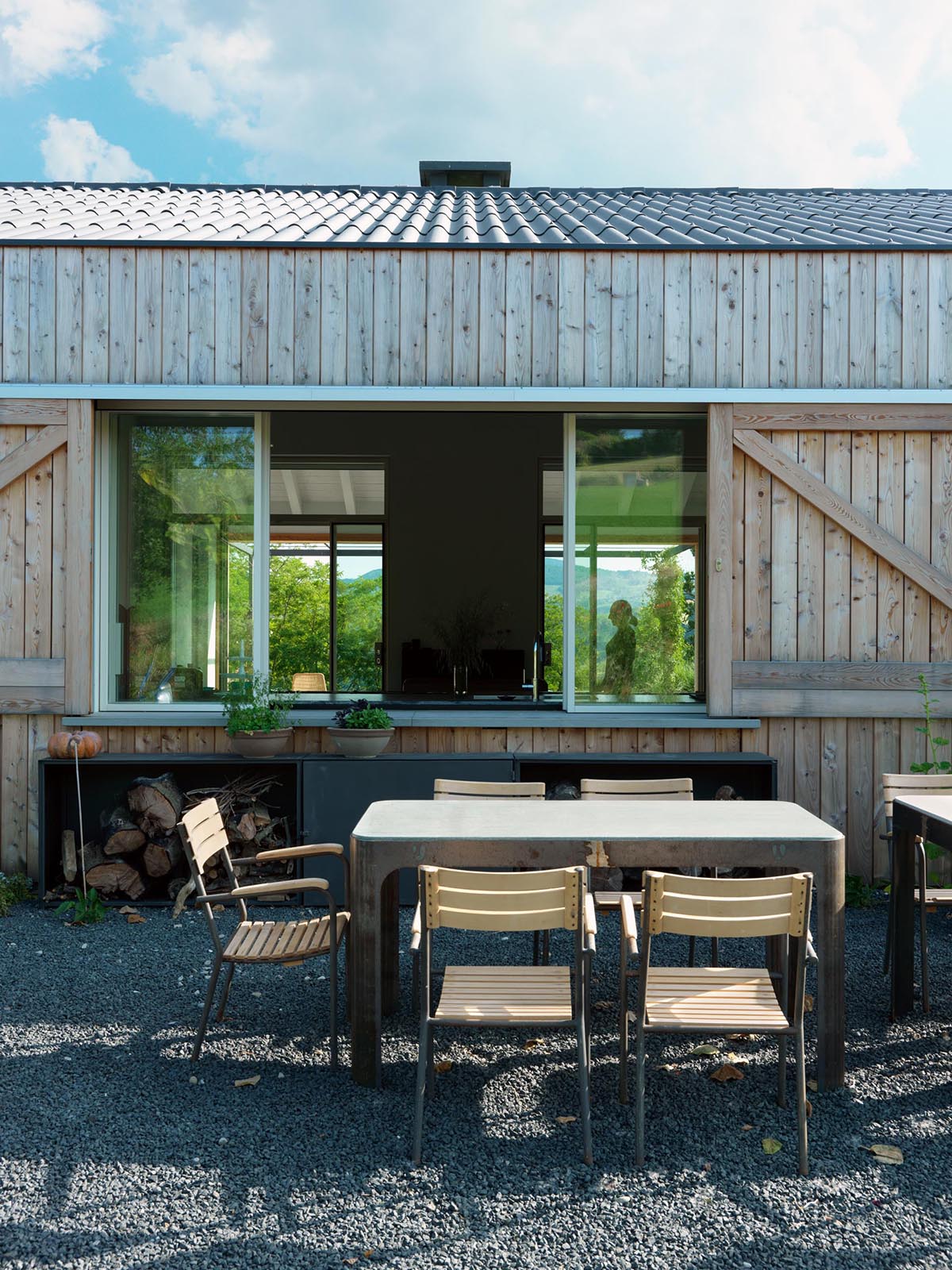 Современный загородный дом с обеденной зоной на открытом воздухе и раздвижными окнами, которые ведут в кухню.