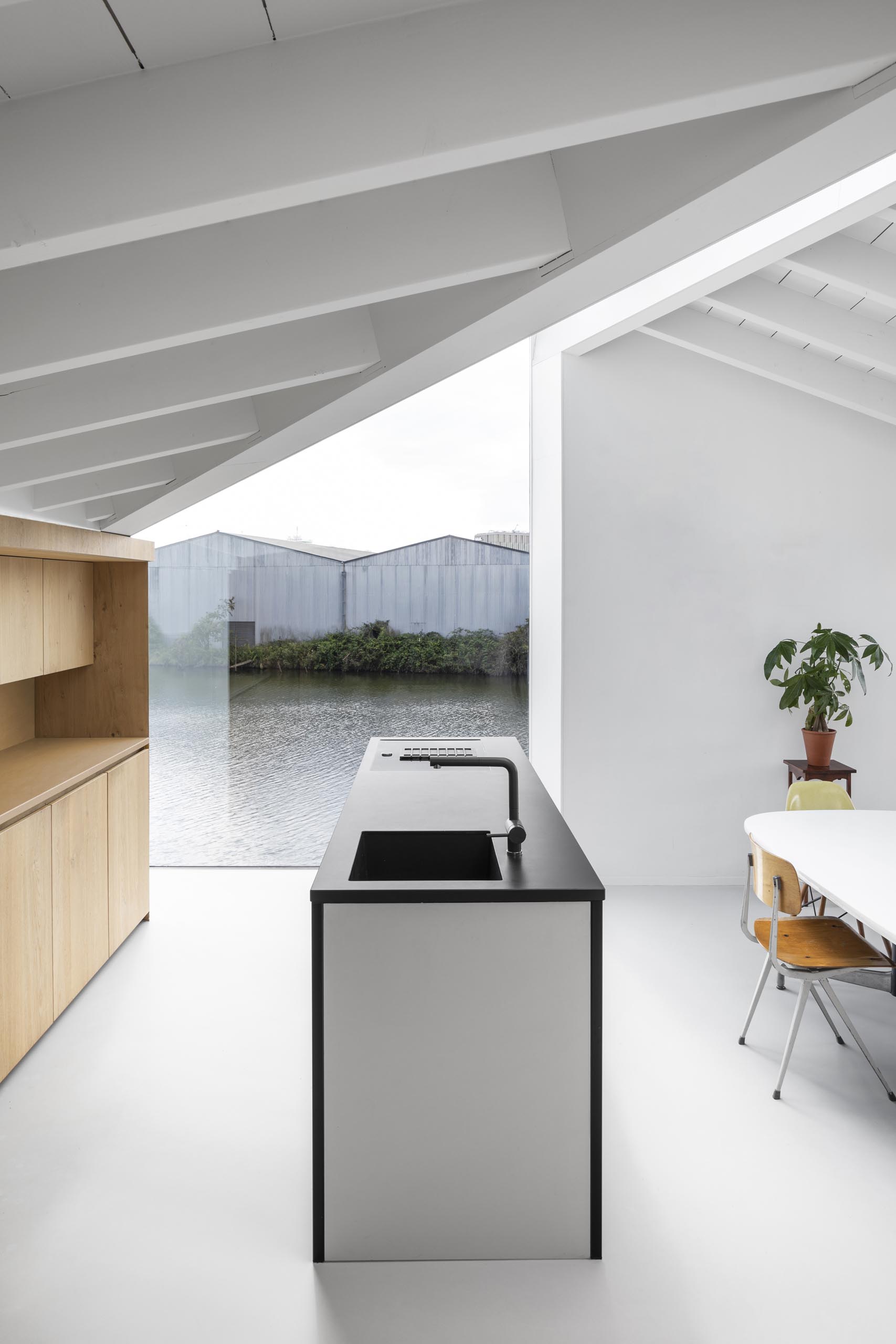 На кухне современного плавающего дома стену из деревянных шкафов дополняет остров с черной столешницей. Обилие окон помогает сохранять интерьер светлым и открытым.