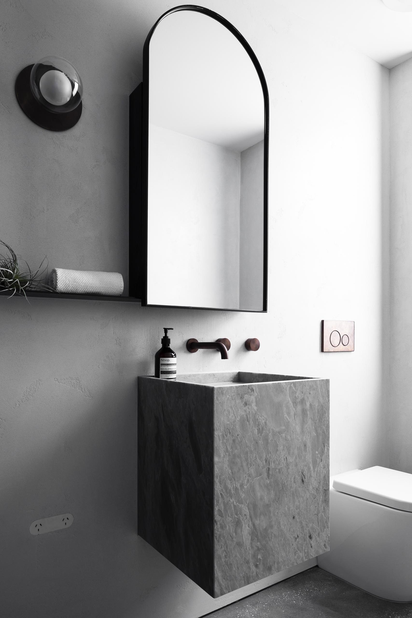 Серая ванная комната с арочным зеркалом в черной рамке и плавающим туалетным столиком.