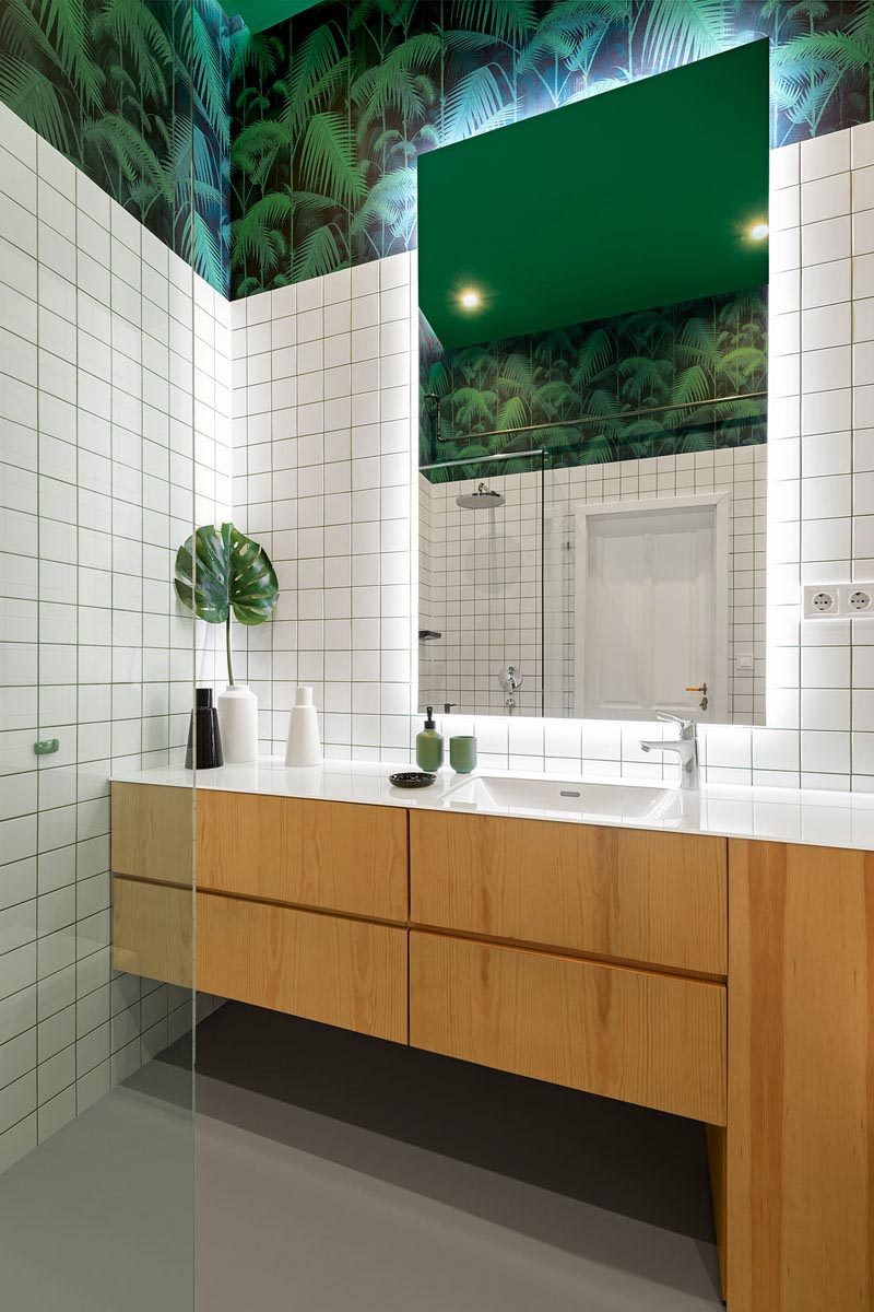 Эта современная ванная комната украшена квадратной белой плиткой, деревянным туалетным столиком, декоративным покрытием стен в виде пальмового дерева и зеркалом с подсветкой. # Ванная # Современная # ЗеленаяБелаяВанная