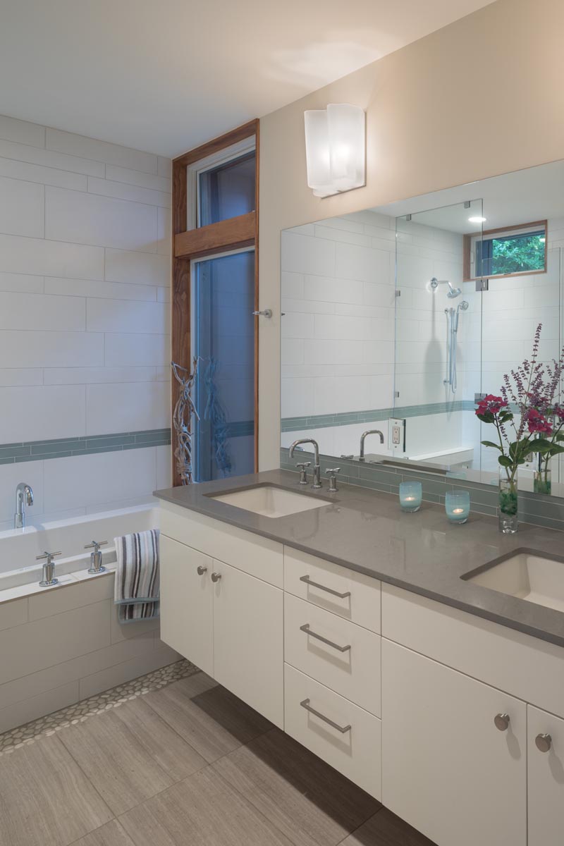 В этой современной ванной комнате белый туалетный столик с двойной раковиной увенчан серой столешницей, а белая плитка, примыкающая к ванной, имеет цветную полосу. # ВаннаяДизайн # БелаяВанная