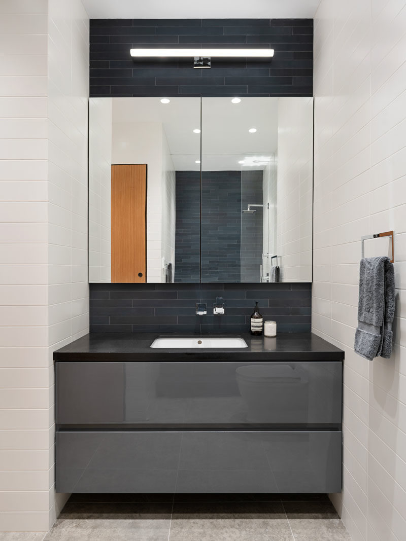 Идеи для ванных комнат - эта современная ванная комната отличается глянцевой серой лаковой раковиной, а темная тонкая плитка, уложенная горизонтально, контрастирует с белой плиткой метро. #BathroomIdeas #BathroomVanity # VanityIdeas # GreyCabinets # ModernBathroom
