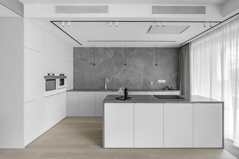 Эта современная кухня демонстрирует минималистские белые шкафы, серые столешницы и серый фартук, покрывающий стену. #ModernWhiteKitchen #ModernKitchen #GreyCountertops