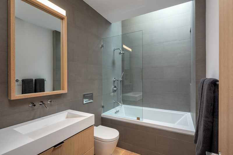 Современная ванная комната с серой плиткой на стенах, элементами из светлого дерева и потолочным окном.