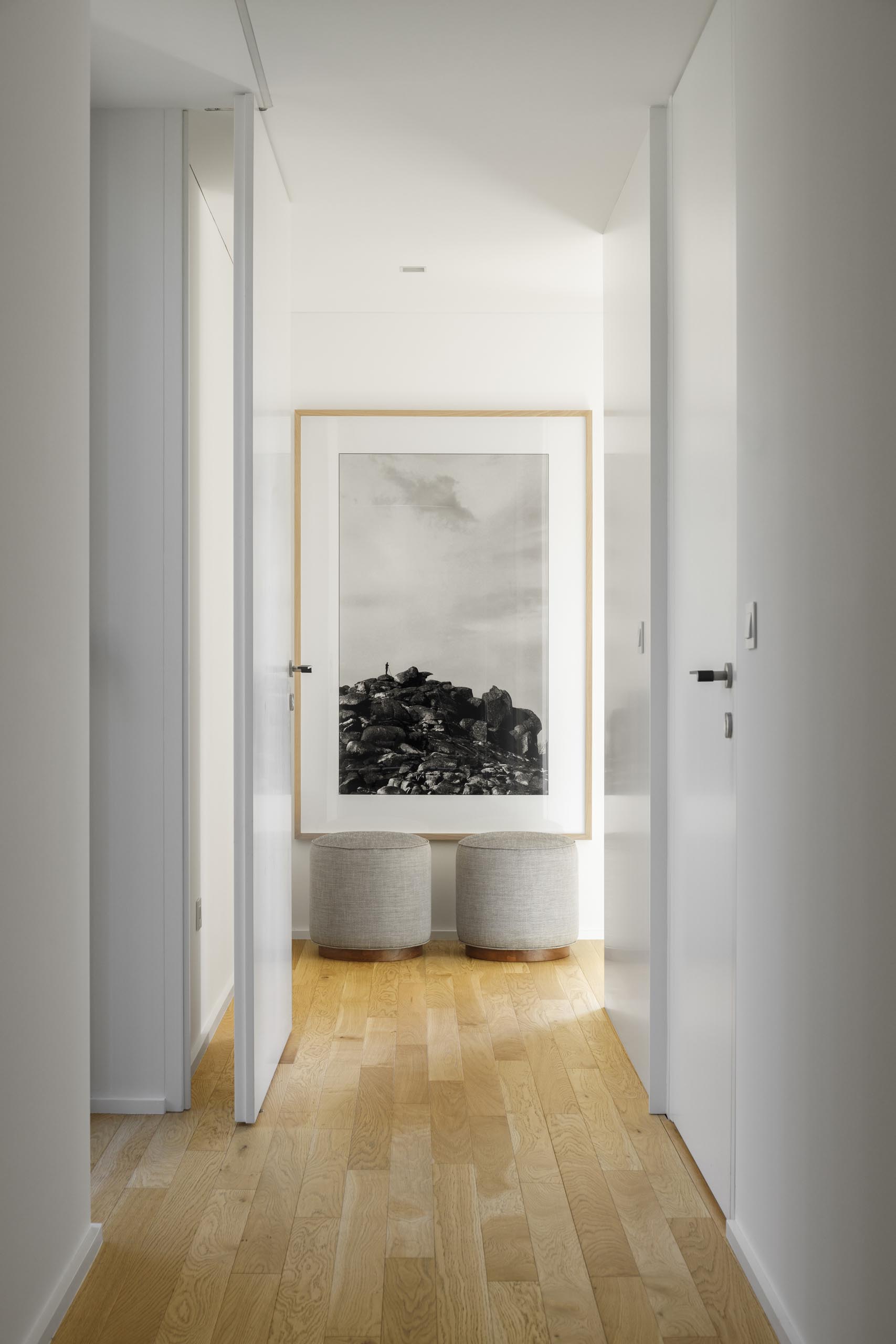 Современный белый коридор с деревянными полами и большим вертикальным принтом.
