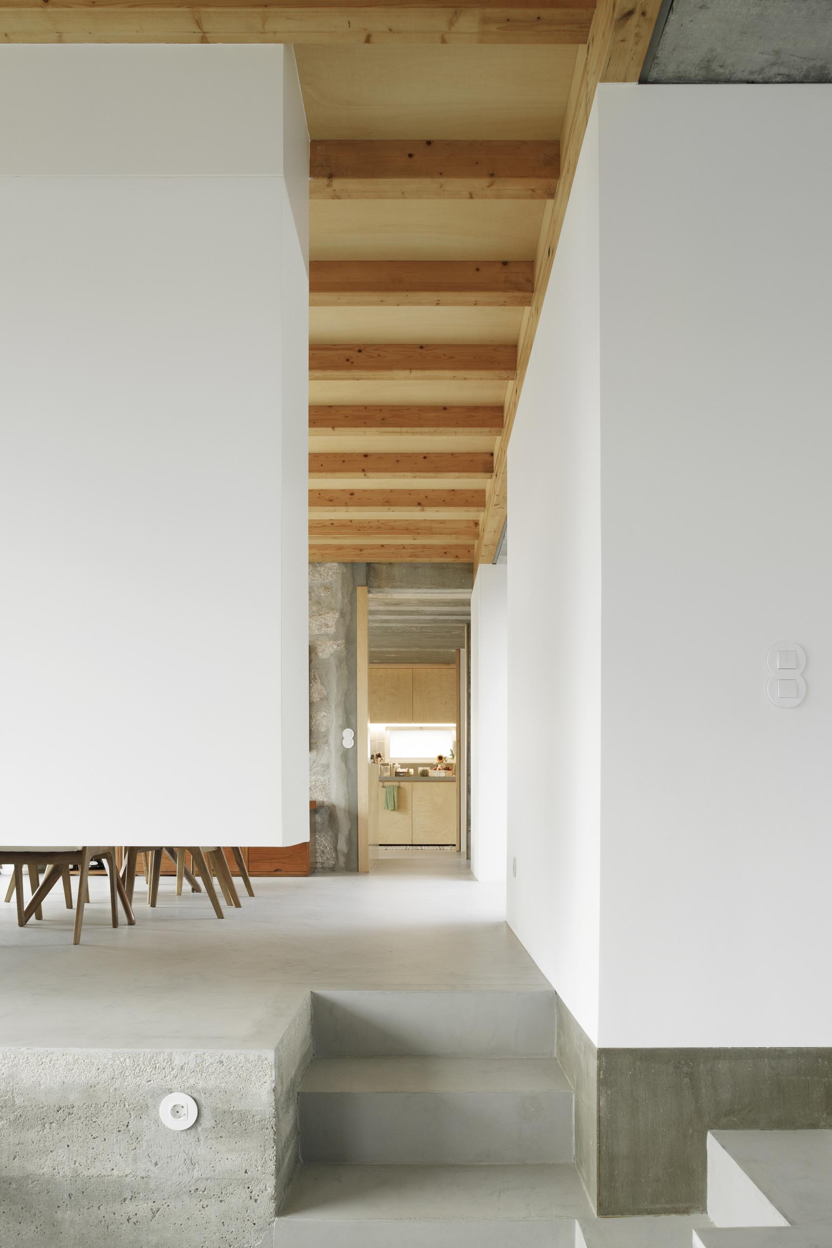 Современный дом с бетонным полом, белыми стенами и деревянным потолком.