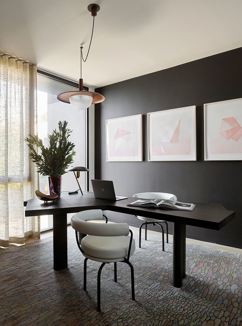 Идеи для домашнего офиса - этот современный домашний офис имеет черную акцентную стену, которая дополняет стол, а светлые произведения искусства и окна от пола до потолка помогают сохранить яркость комнаты. #HomeOfficeIdeas #BlackWall #InteriorDesign