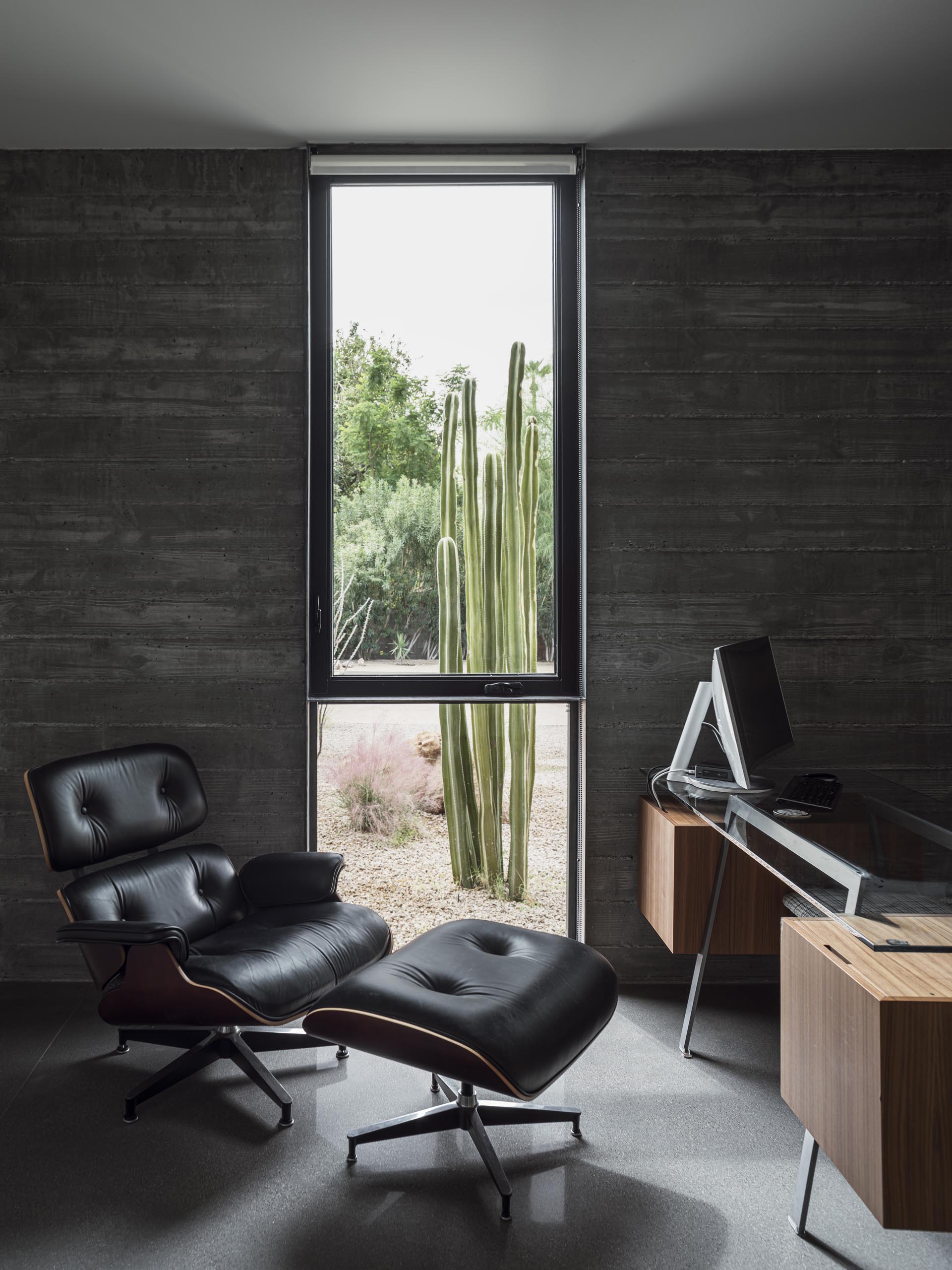 В этом домашнем офисе бетонные стены из досок хорошо видны, а окно от пола до потолка прекрасно обрамляет пустынные растения снаружи.